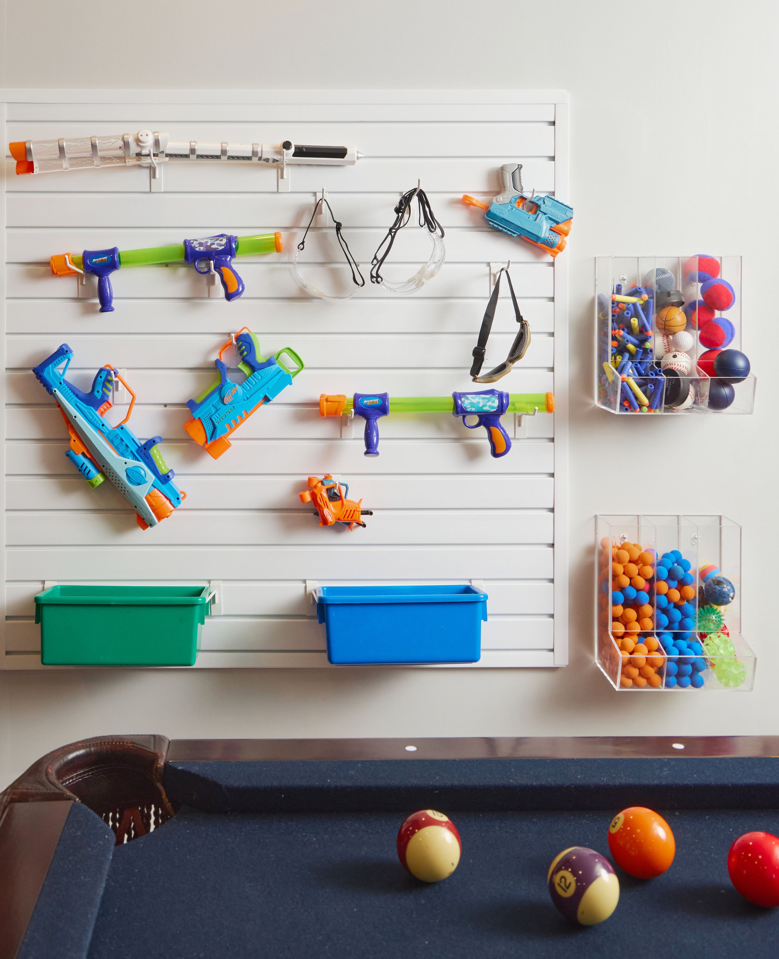 Slatwall toy storage with foam dart blasters, clear ball bins, and colorful baskets above a playroom pool table