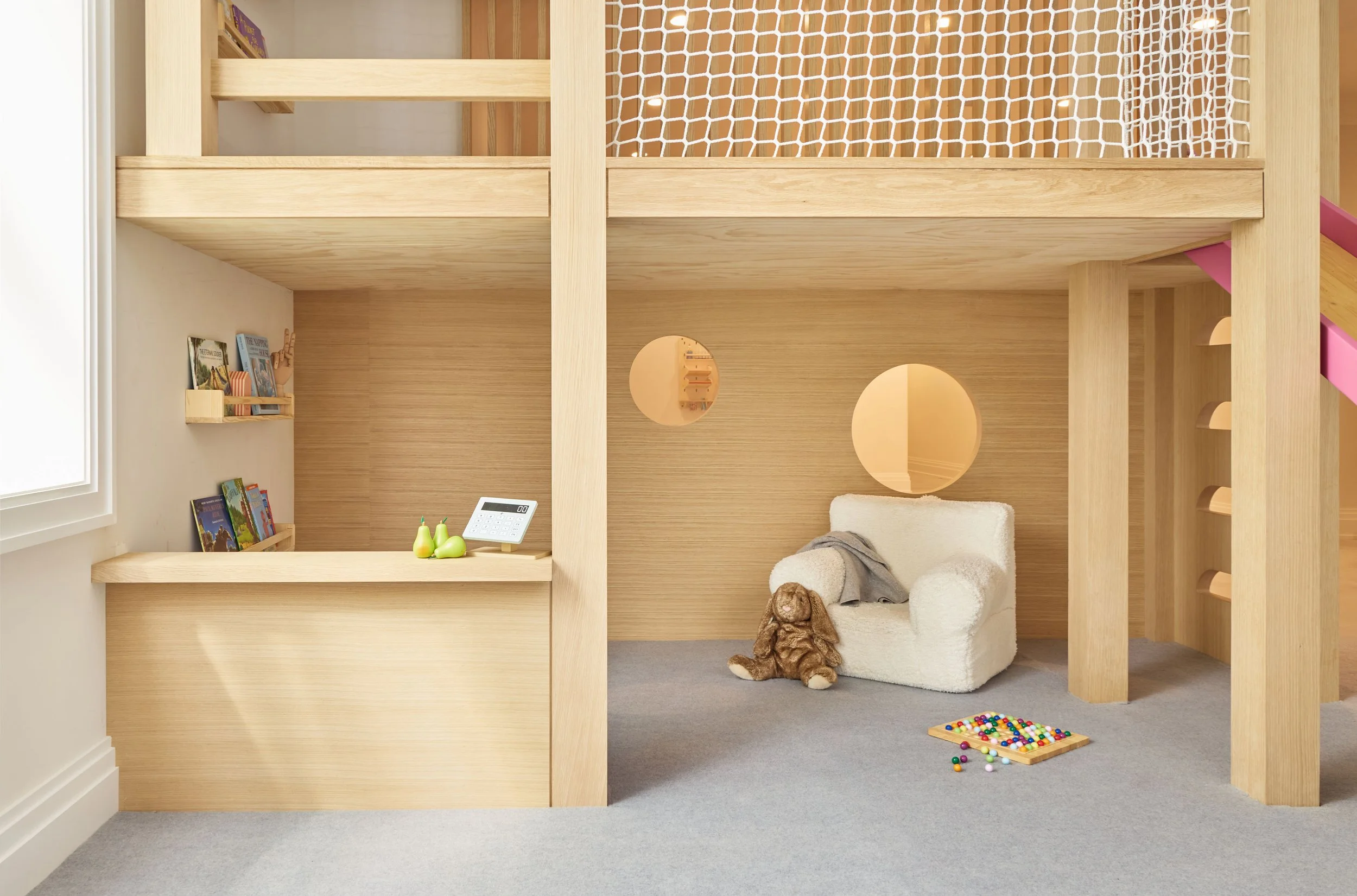 Lower level of a custom white oak kids' play fort with reading nook and built-in book storage