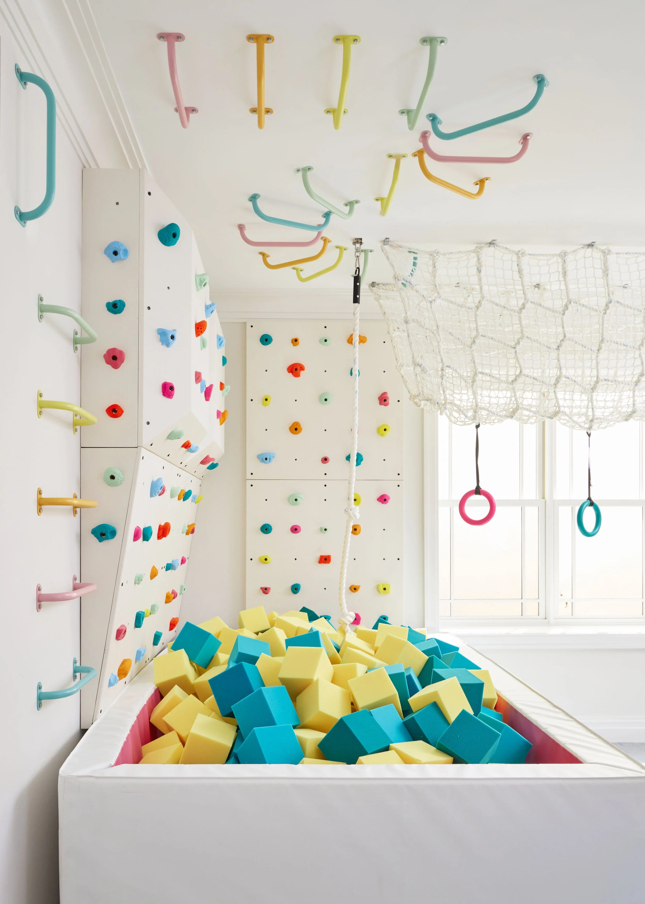 Kids' basement playroom with colorful foam pit, indoor climbing wall and ceiling-mounted monkey bars