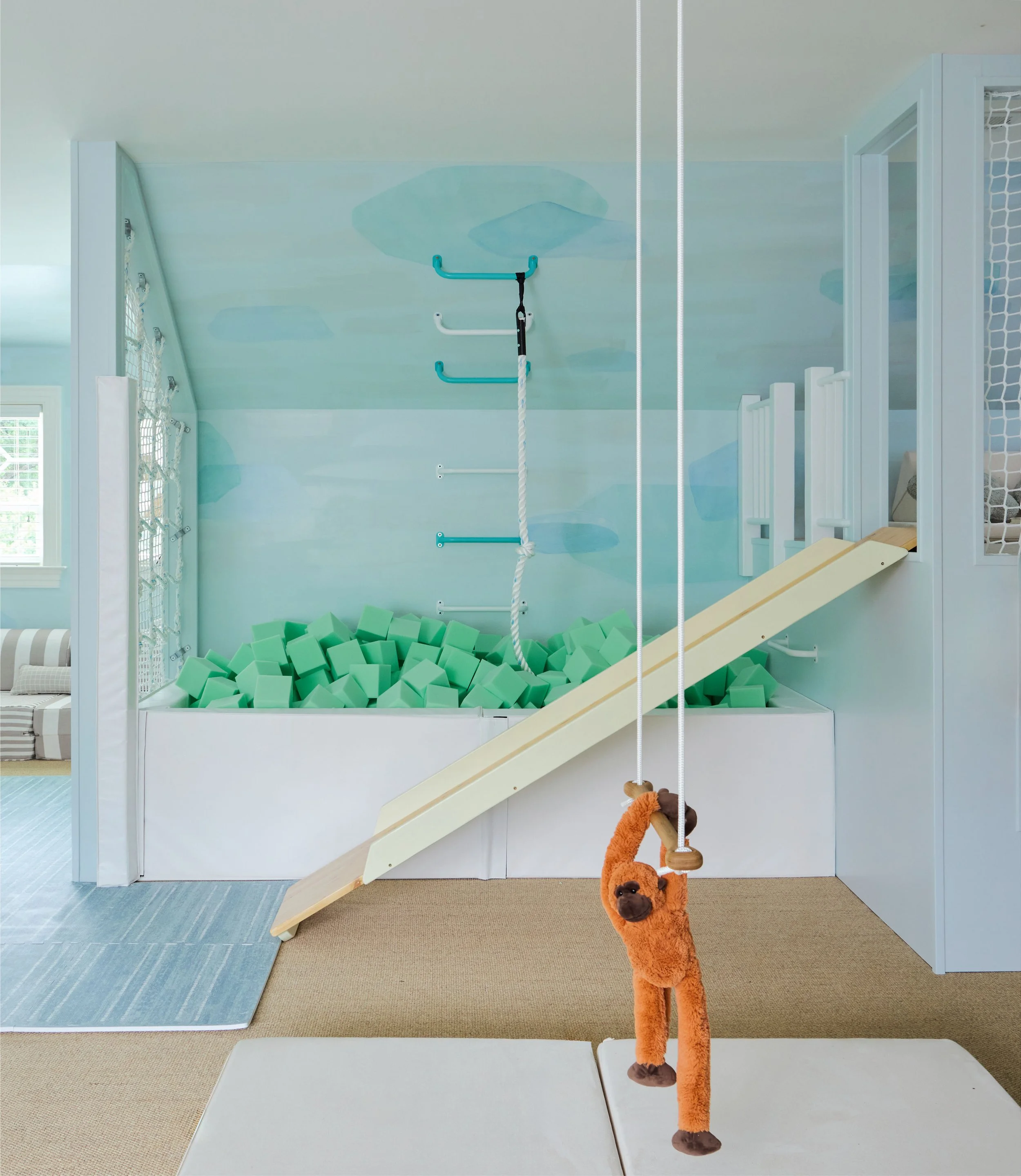 Plush monkey on trapeze bar in foreground with foam pit and slide in background