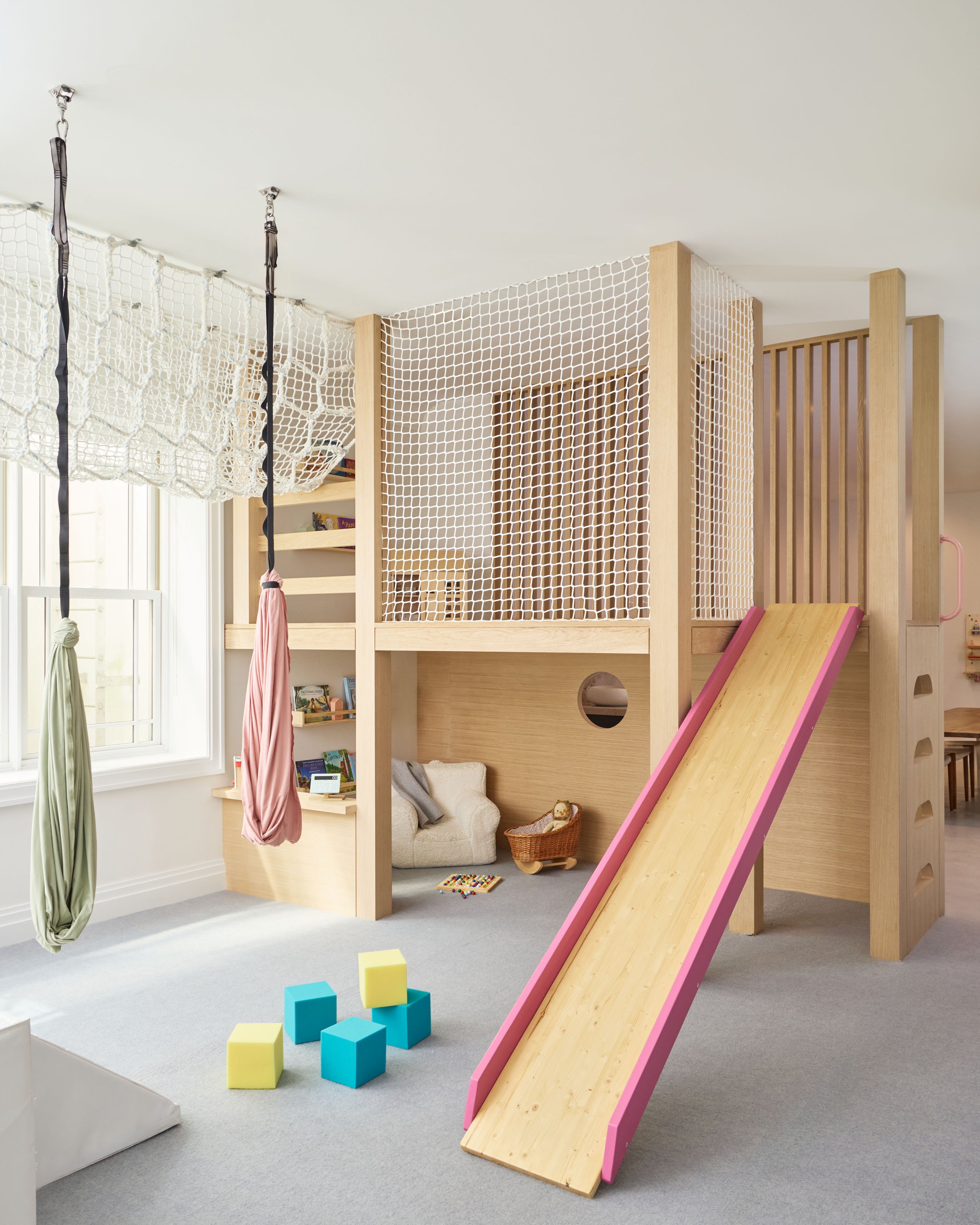 Custom white oak kids' climbing fort with slide in a luxury basement playroom