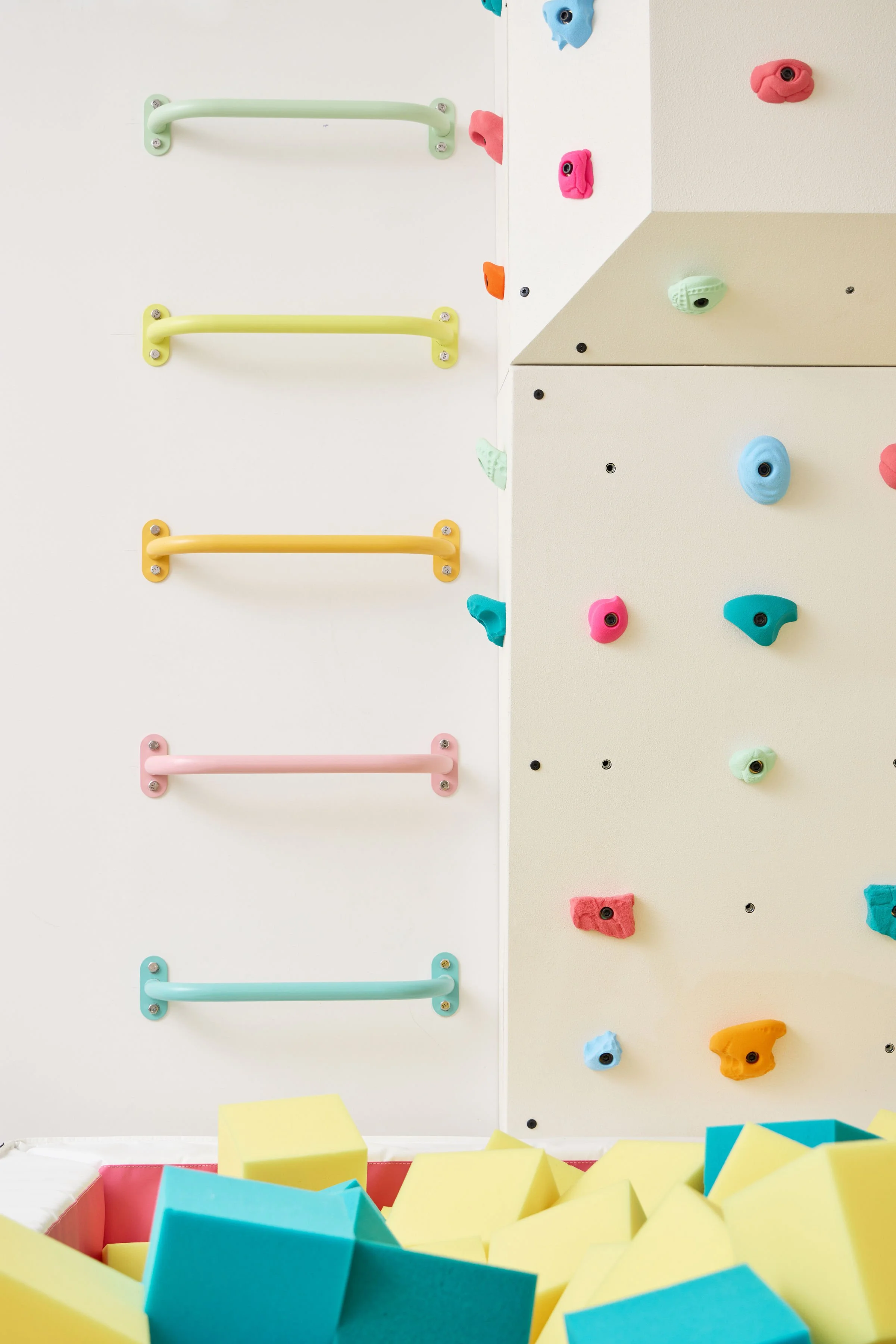 Sherbet-colored wall-mounted monkey bars beside an indoor climbing wall and foam pit