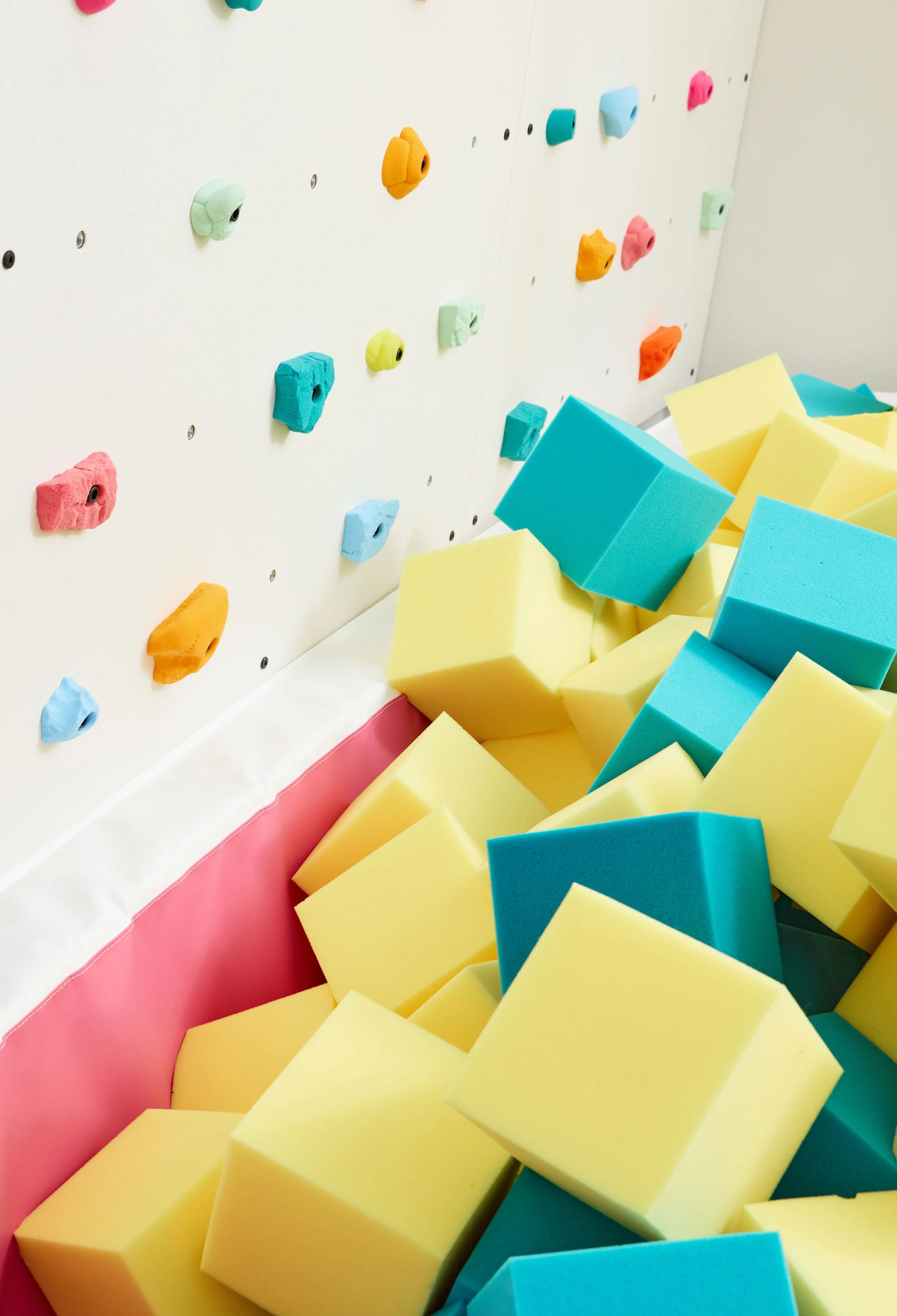 Colorful foam cubes in a kids' foam pit beneath an indoor climbing wall