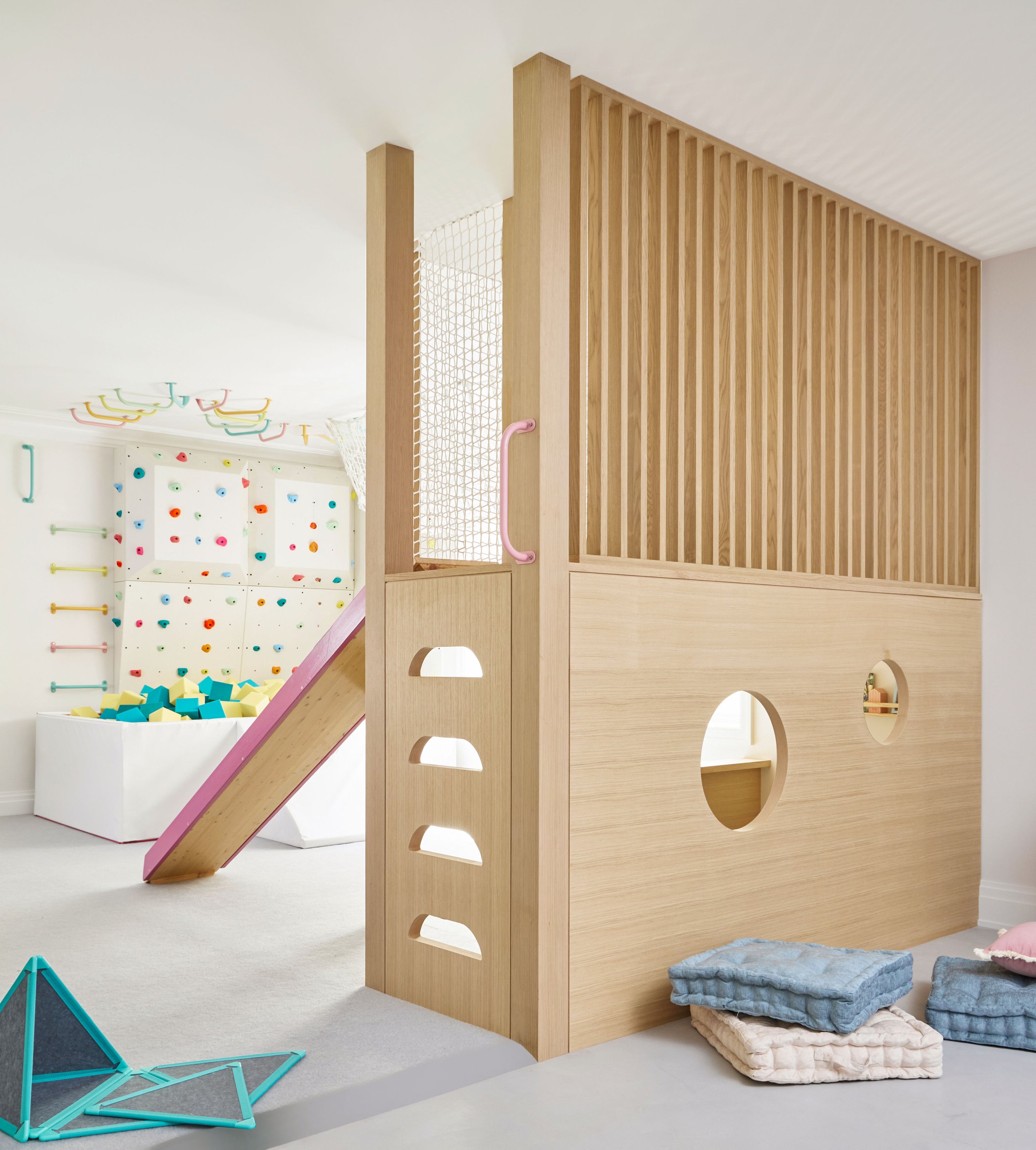 Custom white oak kids' play fort with cutout windows, slide and indoor climbing wall in the background