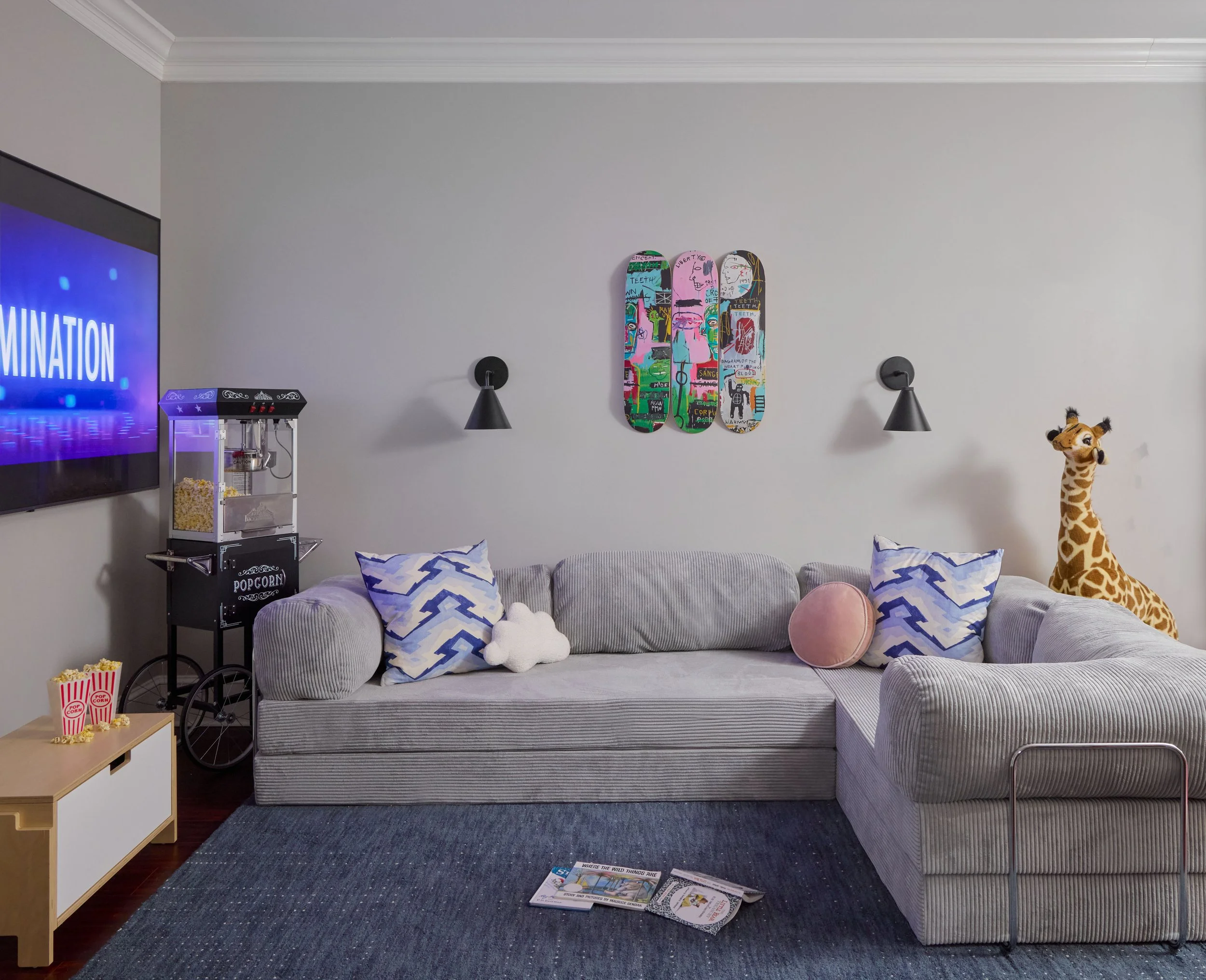 Kids' media lounge with grey sectional sofa, patterned pillows, navy rug, and skateboard wall art