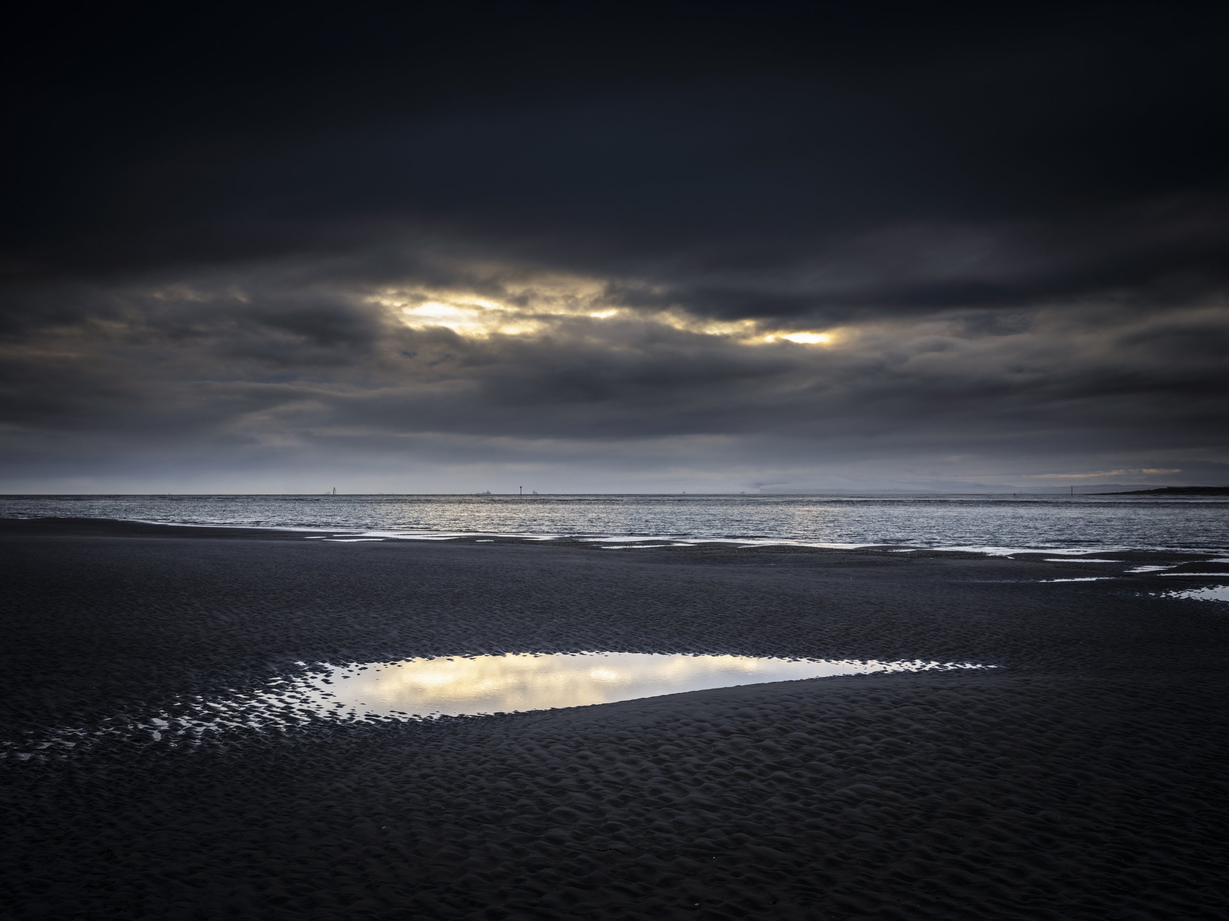 The Calm Beneath the Storm - a small pool of calm water at low tide reflects the light in the stormy sky.
