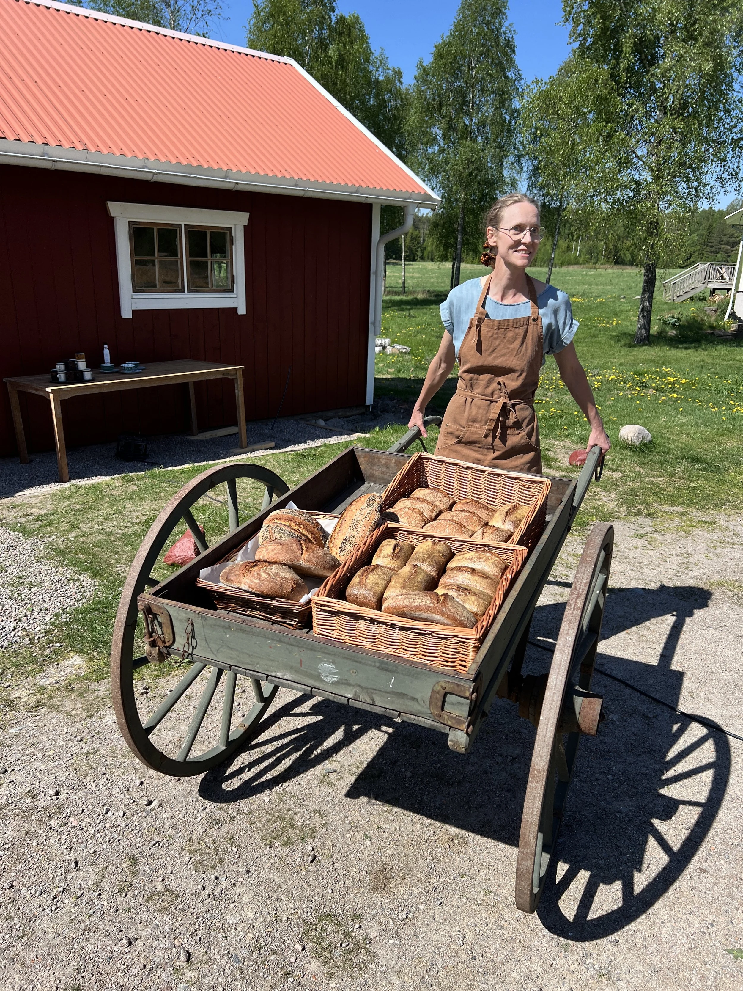 Ett lass med nybakade bröd på en gammal träkärran utomhus med en röd liten stuga i bakgrunden