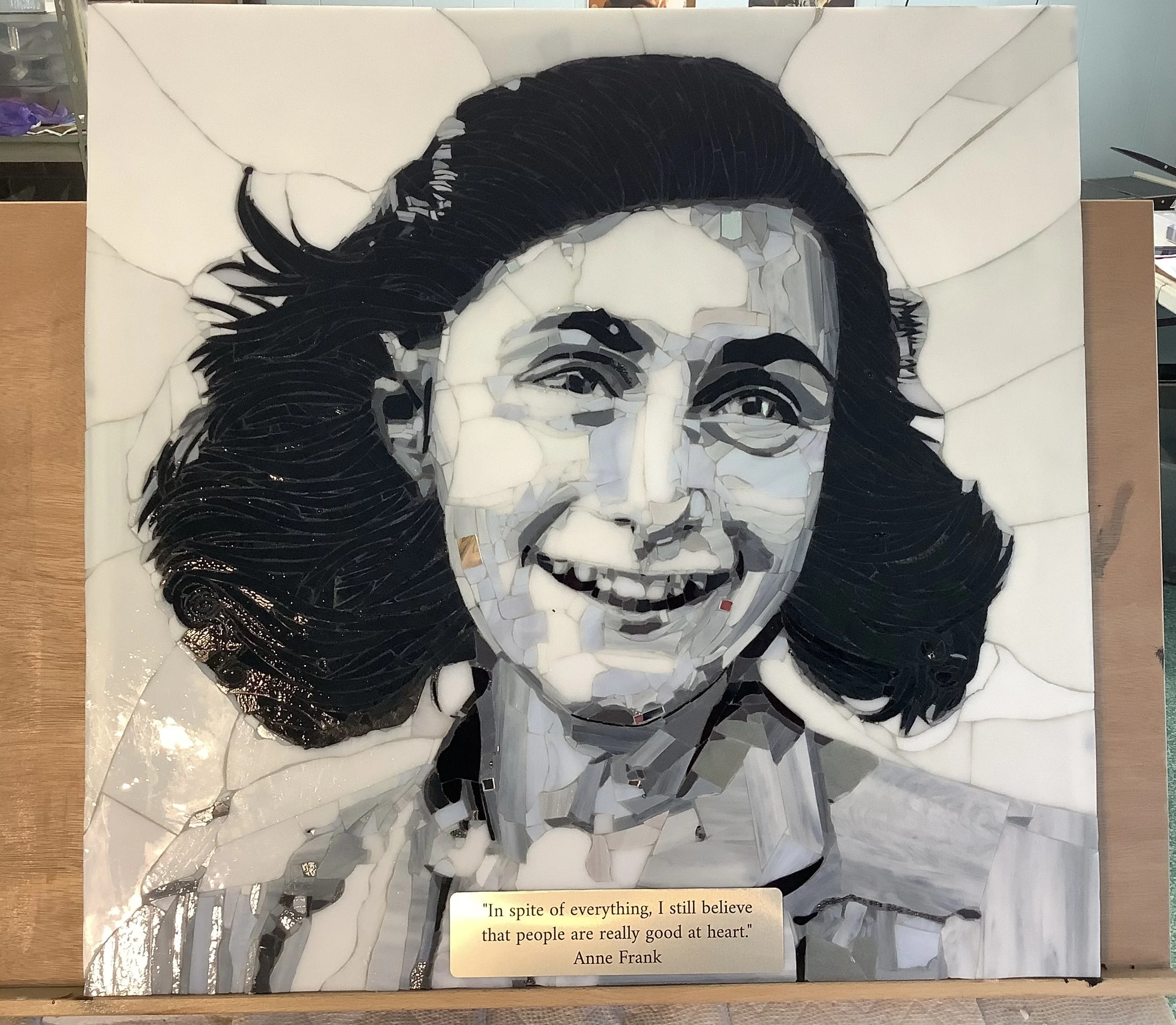 A mosaic artwork of Anne Frank's portrait made from various materials, with a quote at the bottom that reads: "In spite of everything, I still believe that people are really good at heart." - Anne Frank