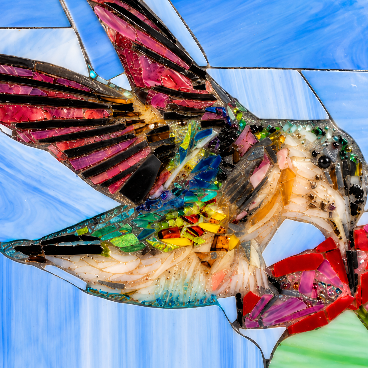 Macro close-up of hummingbird stained glass mosaic showing detailed colorful glass pieces, wings, feathers and flower
