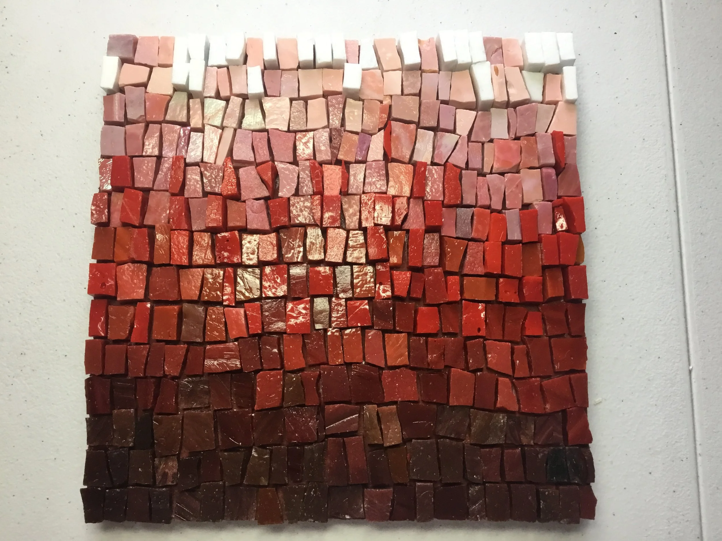 A mosaic of small, square tiles arranged in a gradient from white at the top through pink, red, and dark brown at the bottom.