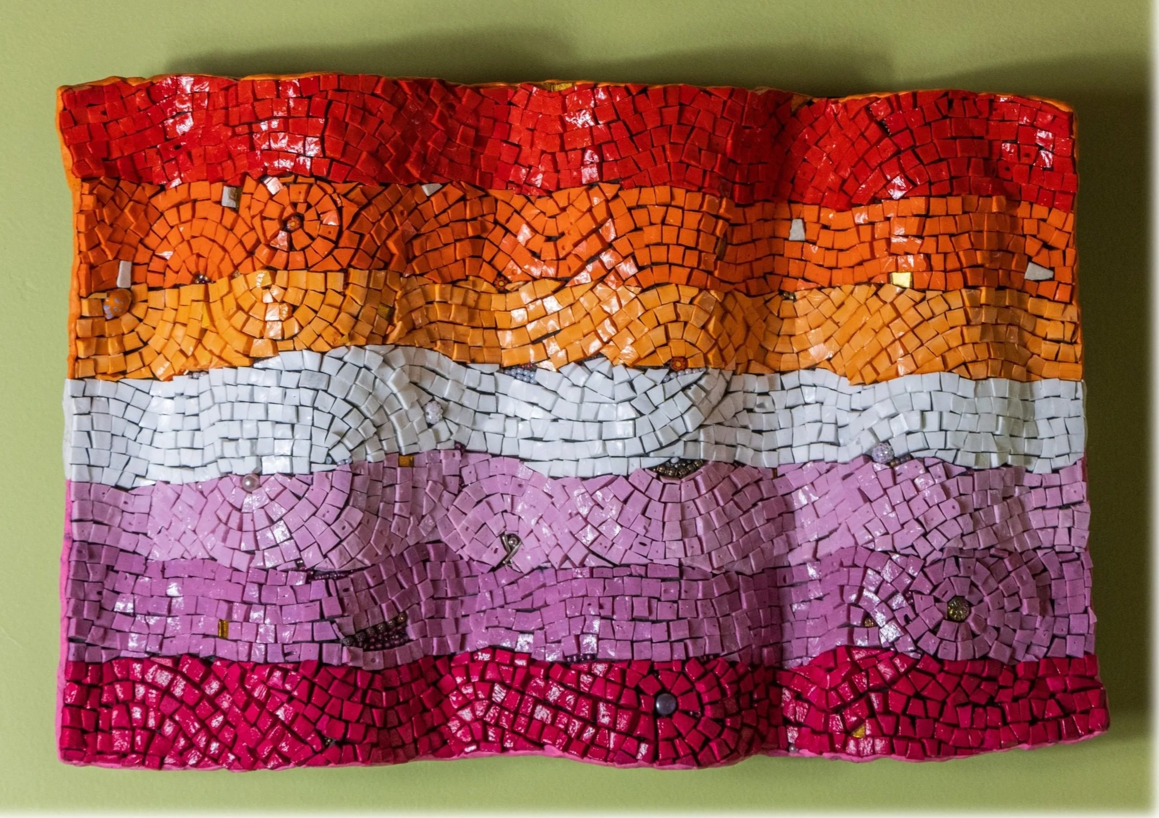 Mosaic artwork with horizontal stripes of red, orange, white, pink, and red tiles on a green background.