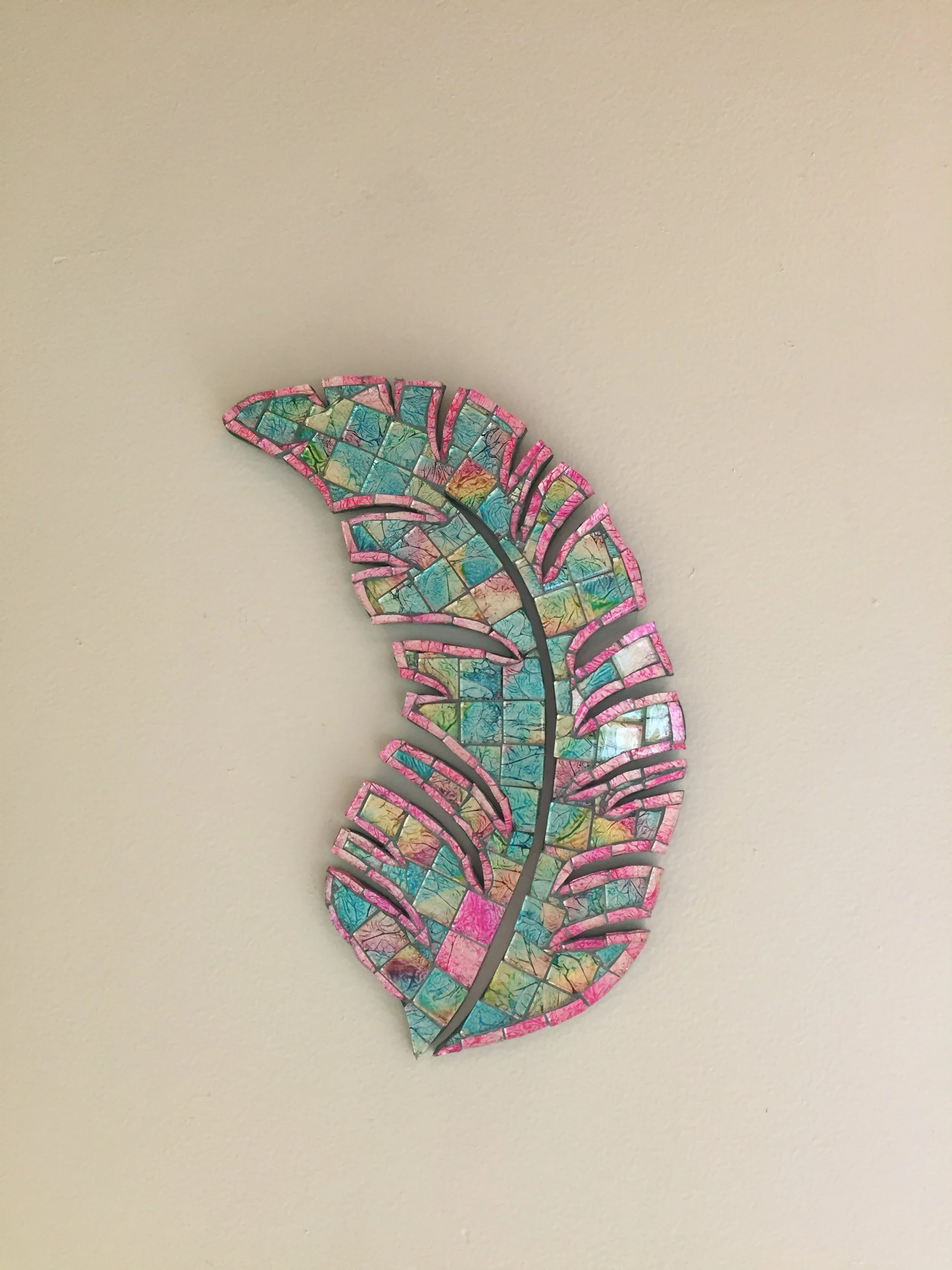 Colorful mosaic art of a tropical leaf mounted on a plain wall.