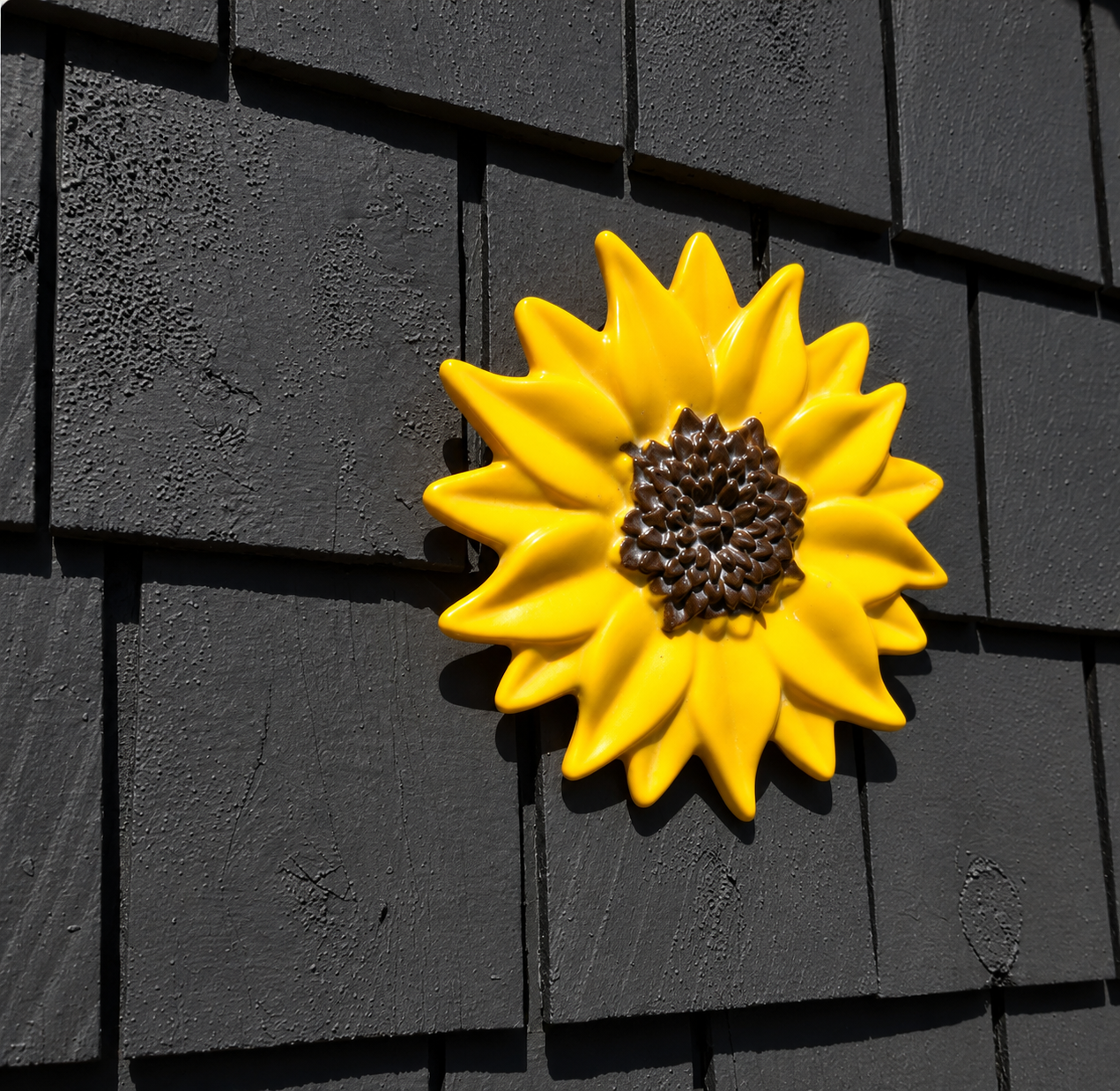Handmade yellow fused glass sunflower wall art with textured brown center displayed on a dark exterior wall