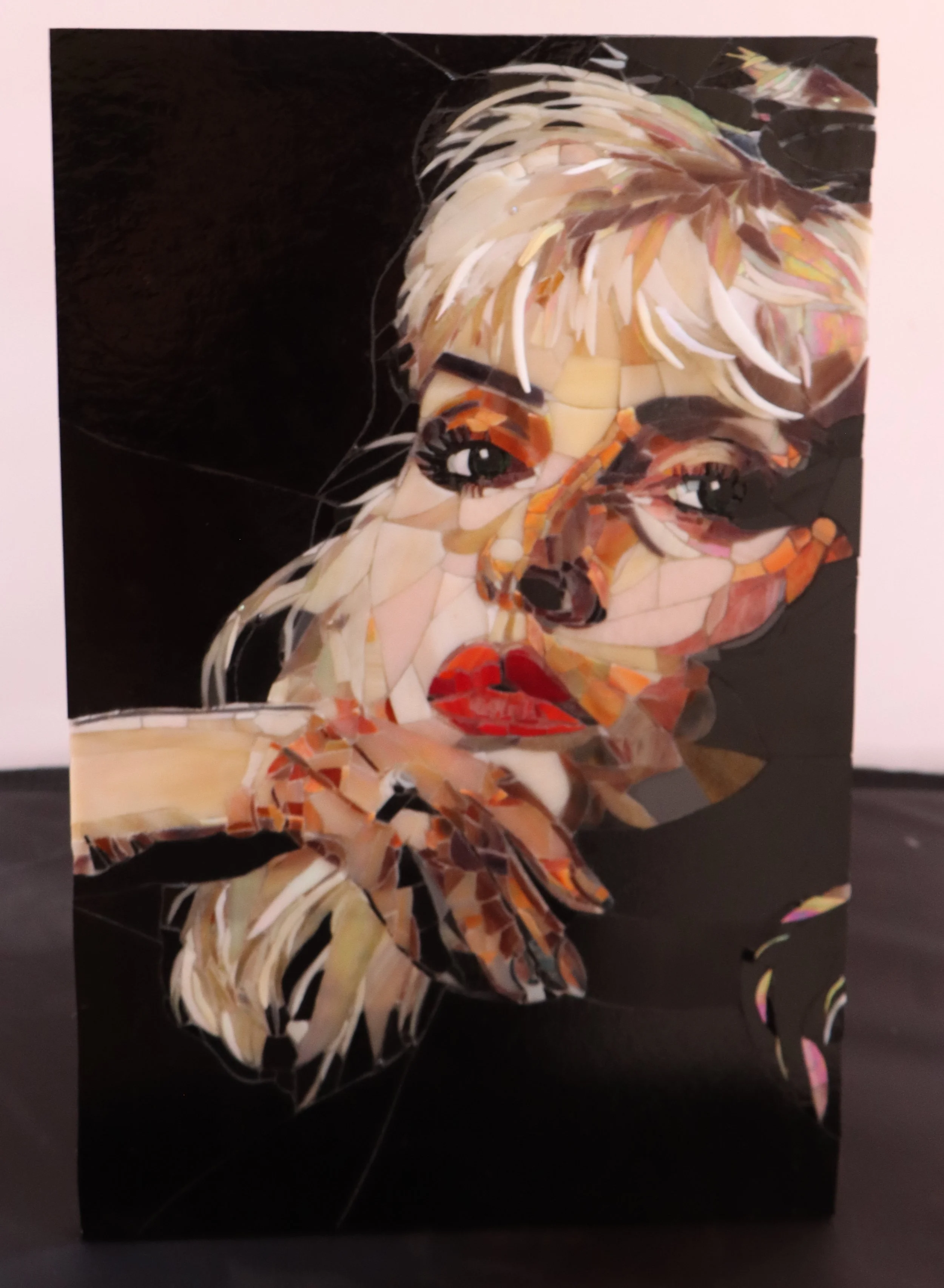 A mosaic art piece of a Debbie Harry ,woman's face with blonde hair, red lips, and expressive eyes, set against a dark background.