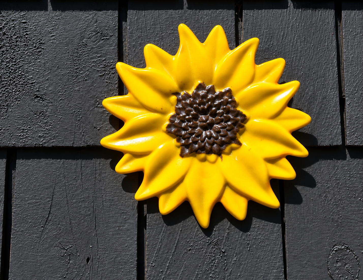 Handmade yellow fused glass sunflower wall art with textured brown center displayed on a dark exterior wall