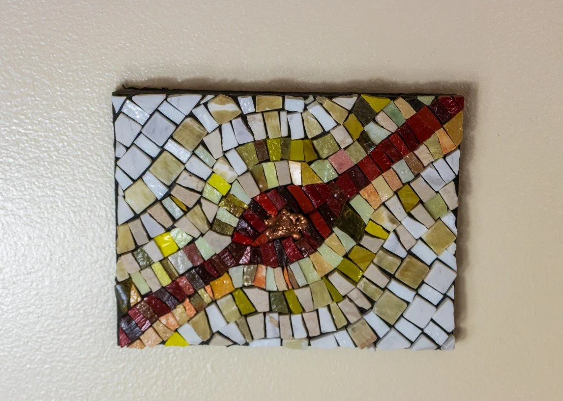 Colorful mosaic wall art with abstract design on a beige wall.