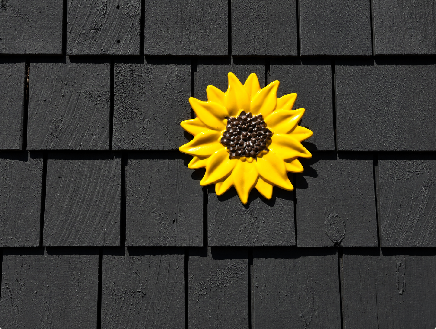 Handmade yellow fused glass sunflower wall art with textured brown center displayed on a dark exterior wall