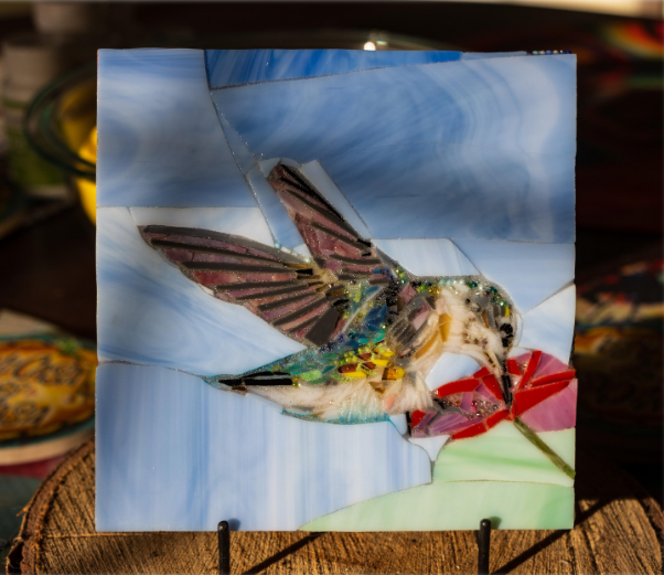 Handmade hummingbird stained glass mosaic art with colorful glass bird and red flower displayed on a black stand