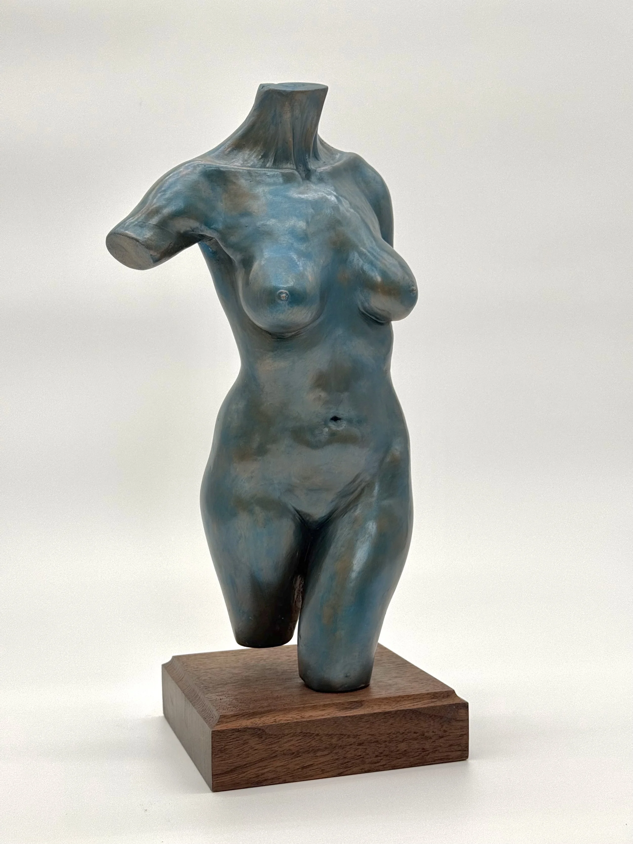 A mixed media sculpture of a female torso, with realistic body features, mounted on a wooden base.