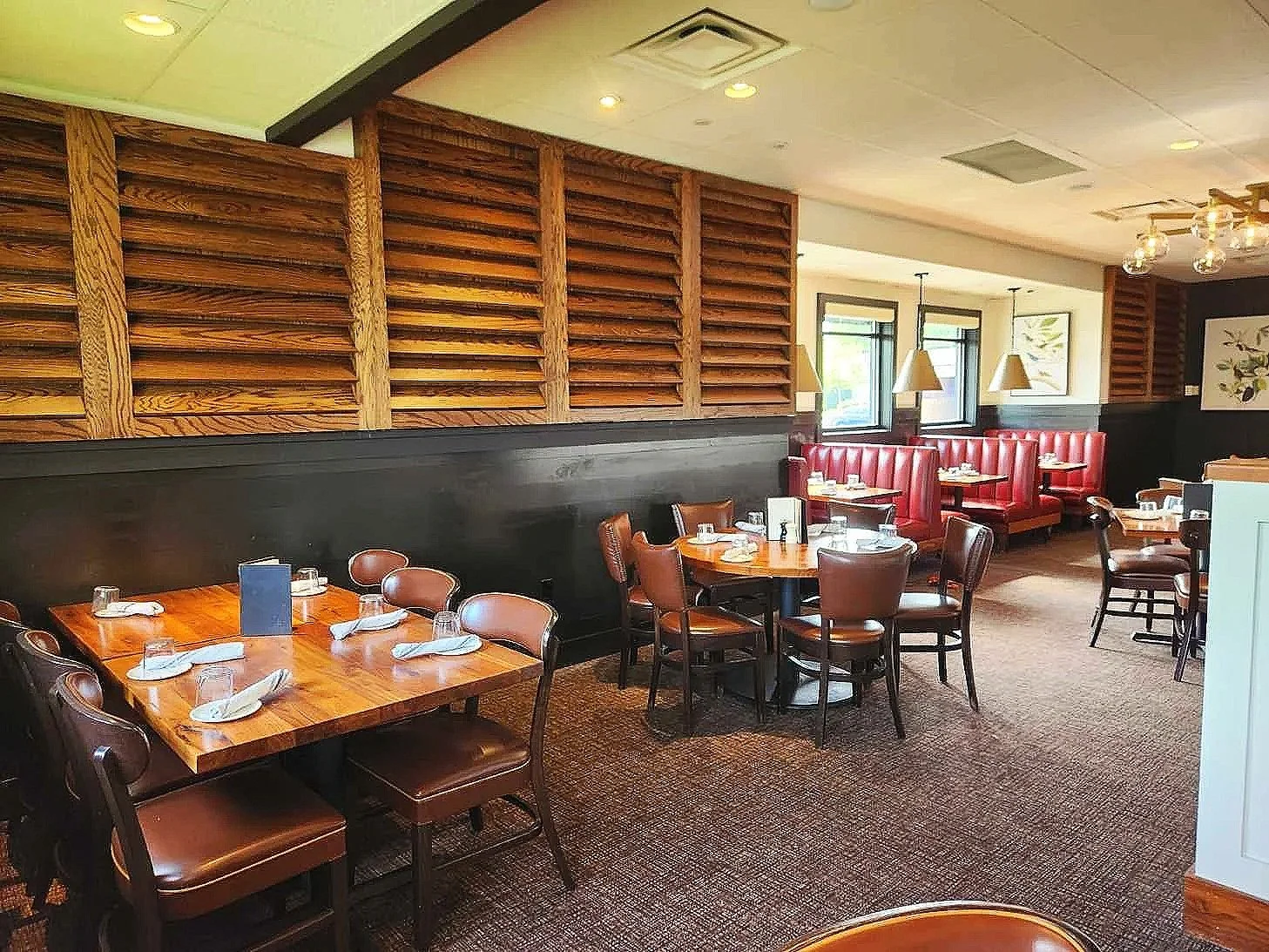 Interior of a restaurant with wooden accents, red booth seating, and tables set with glasses and napkins.