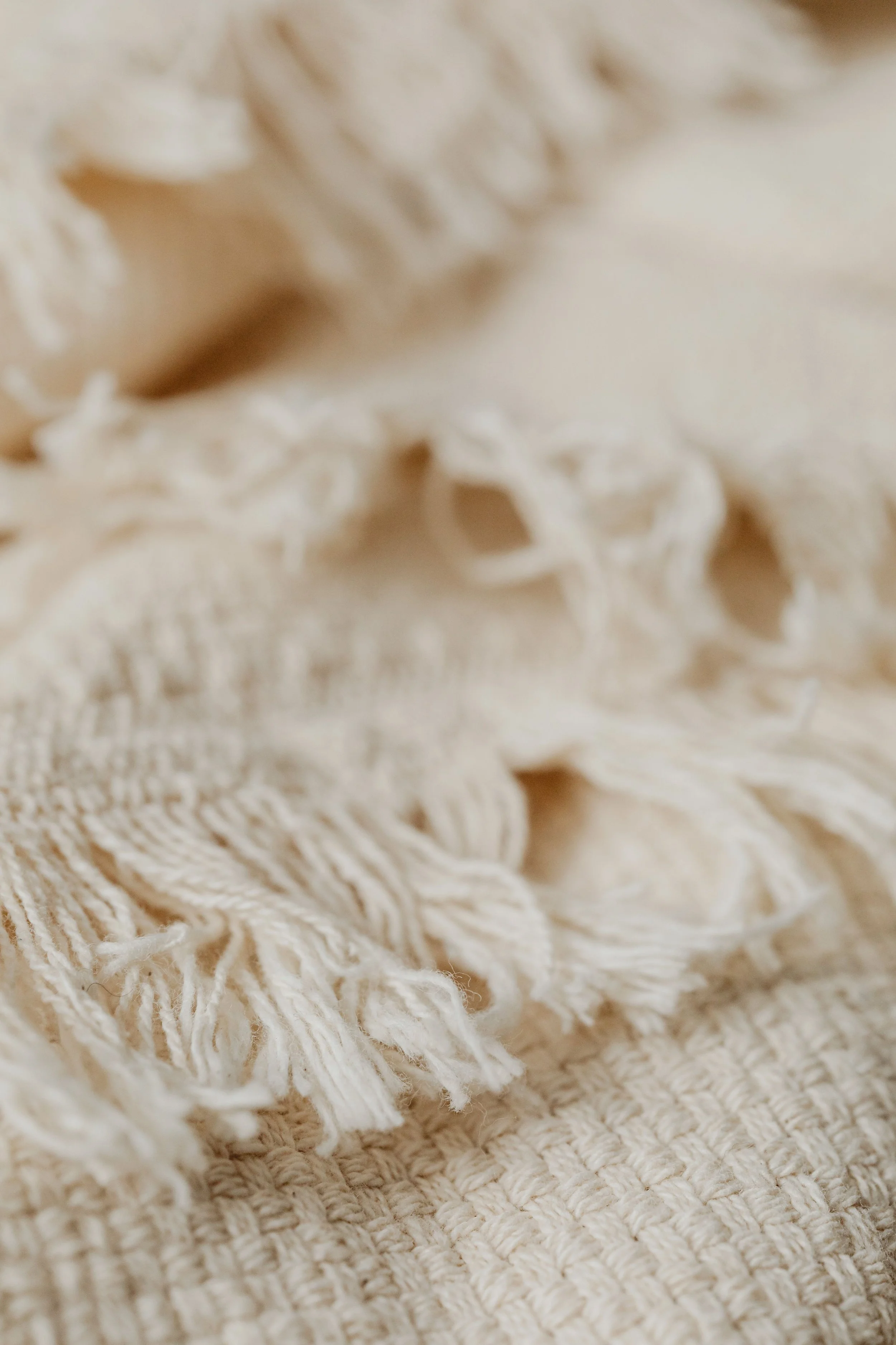 Close-up view of a woven, cream-colored blanket with fringed edges.
