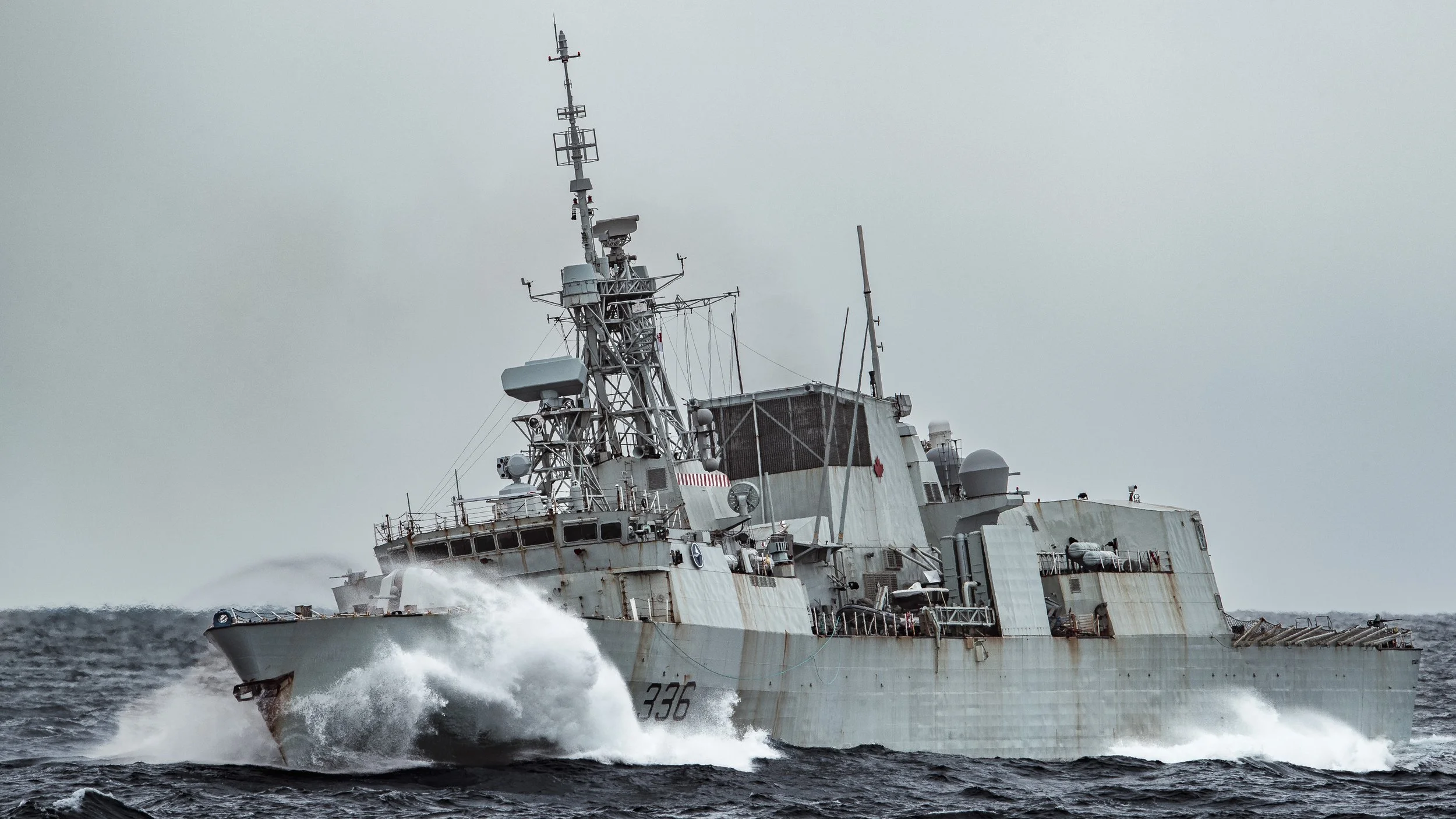 Military ship with the number 336 moving through the ocean with waves and a cloudy sky.