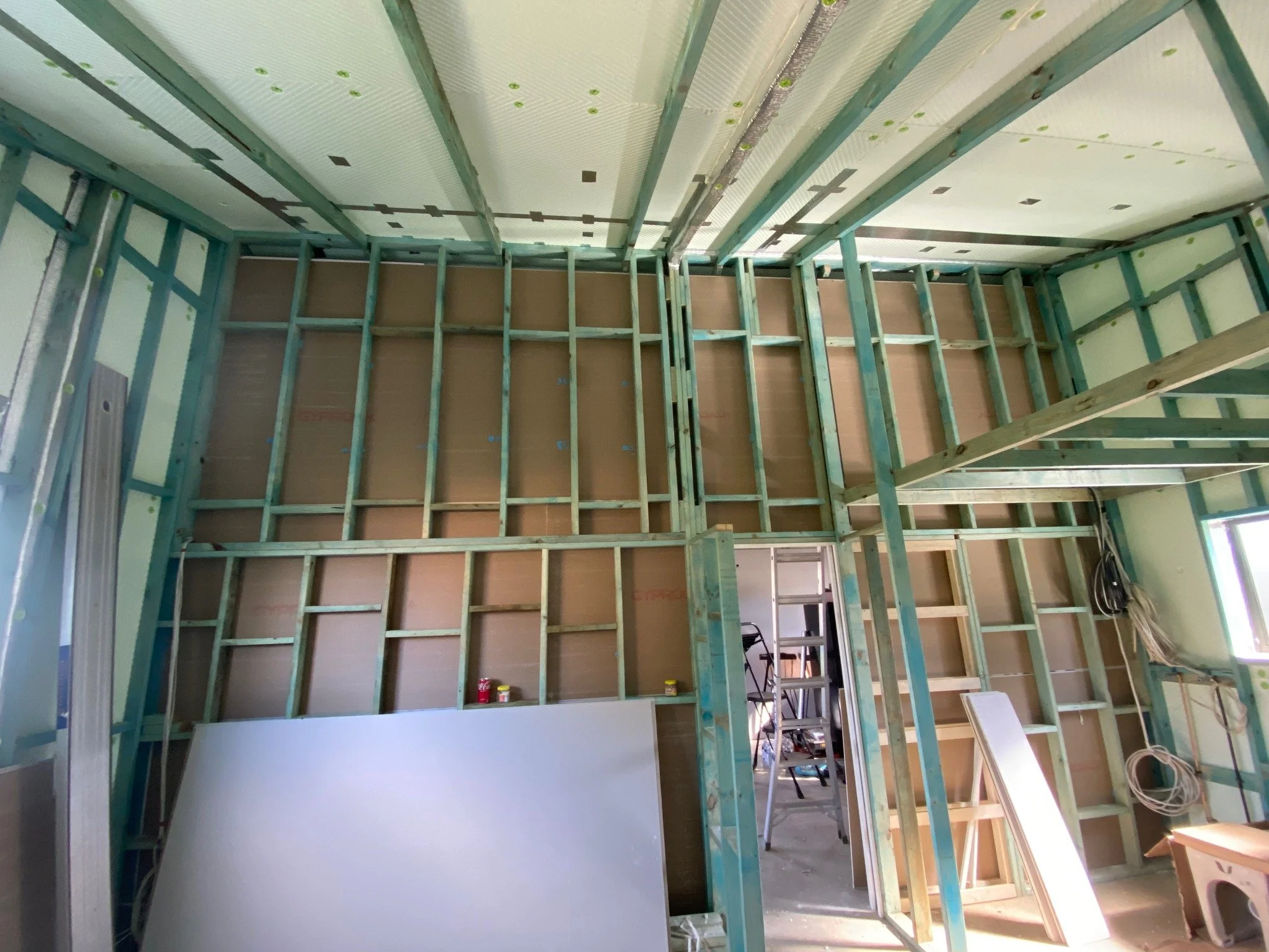 Interior of a room under construction with exposed wooden framing, a ladder, and construction materials.
