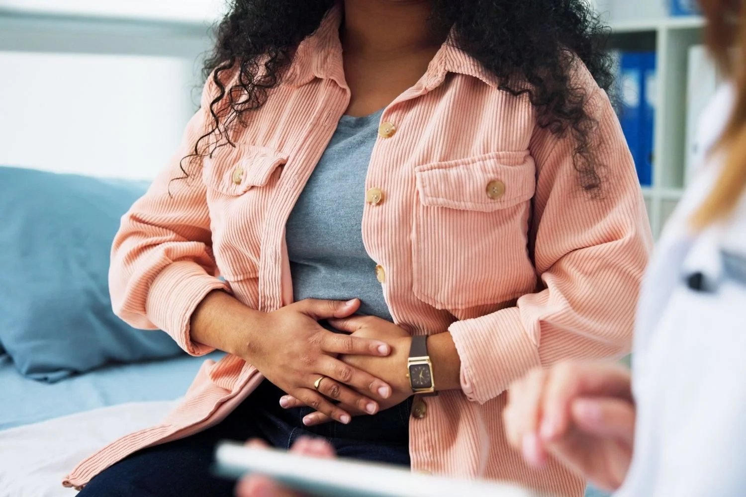 Person clutching their stomach during a medical visit, talking with a healthcare professional.