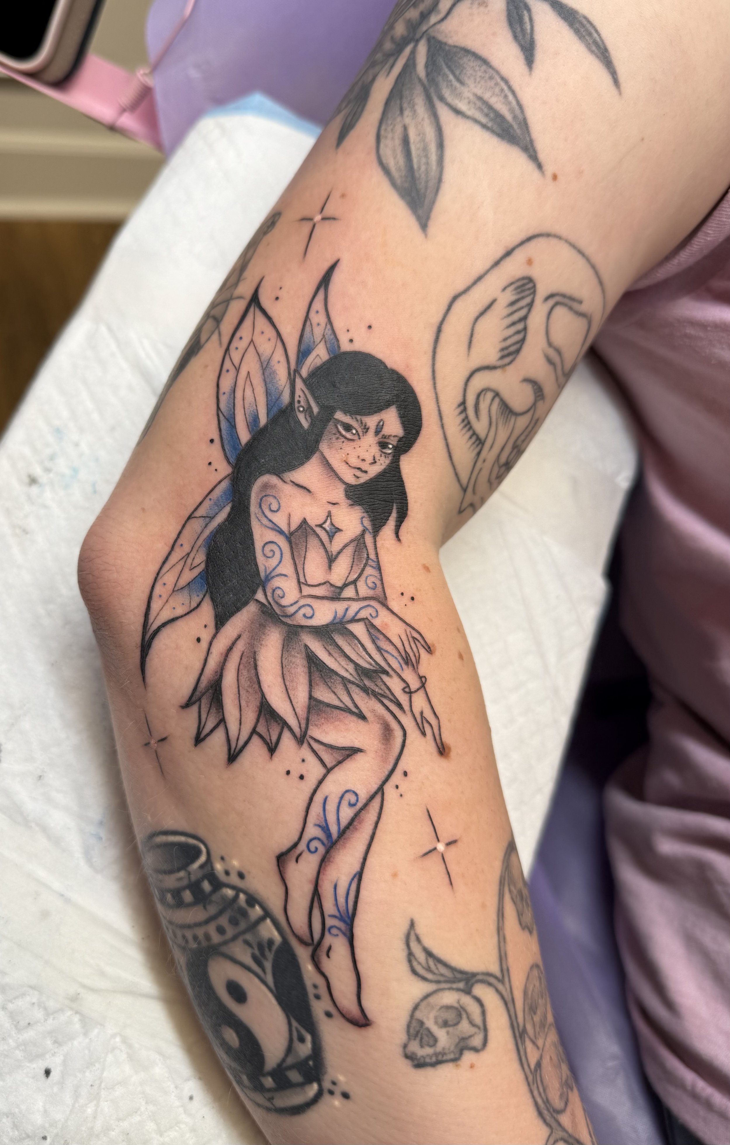 Tattoo of two strawberries with green leaves surrounded by pink flowers with yellow centers on a person's arm. Chelsea Graham illustrative, american traditional, and kawaii tattoo artist seattle washington.