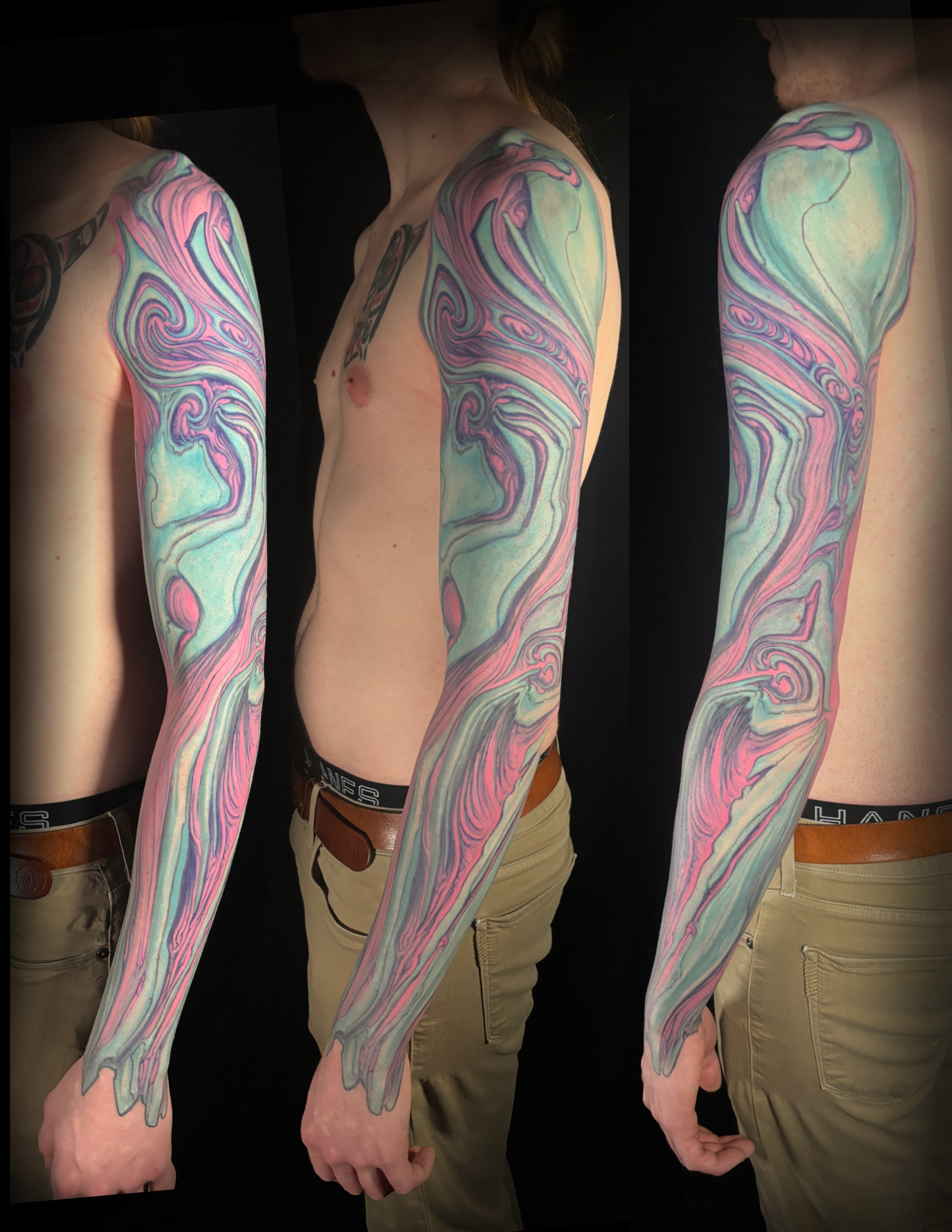 A person with a colorful marbled abstract sleeve tattoo wearing a black sleeveless T-shirt with a graphic of a sunset, palm trees, and the text 'T. RAGNAR AIR SERVICE'. Adam Miller biomechanical tattoo artist