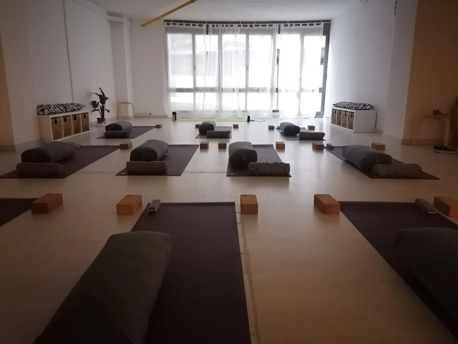 Alquiler Sala de yoga con esterillas, bloques de madera y cojines en un ambiente iluminado con cortinas blancas