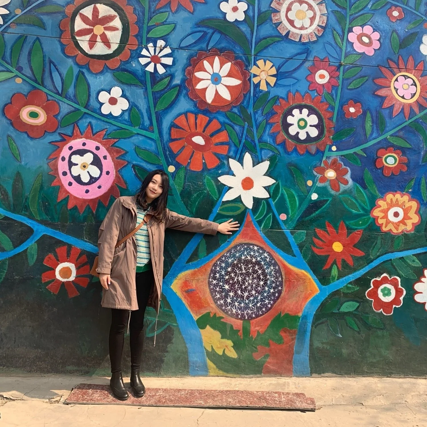 Xueer Arielle Jiang stands in front of the brightly painted Tree of Life Mural at the original Dandelion Middle School campus.