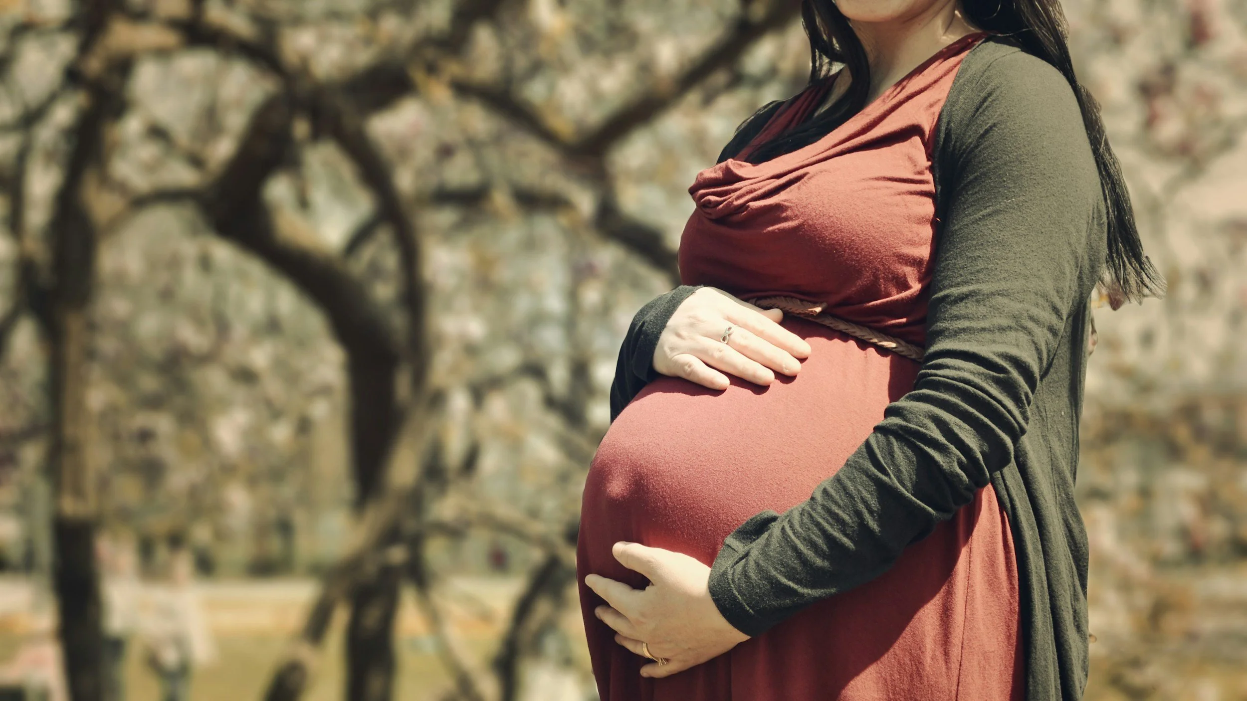 Women holds two hands on pregnant belly.