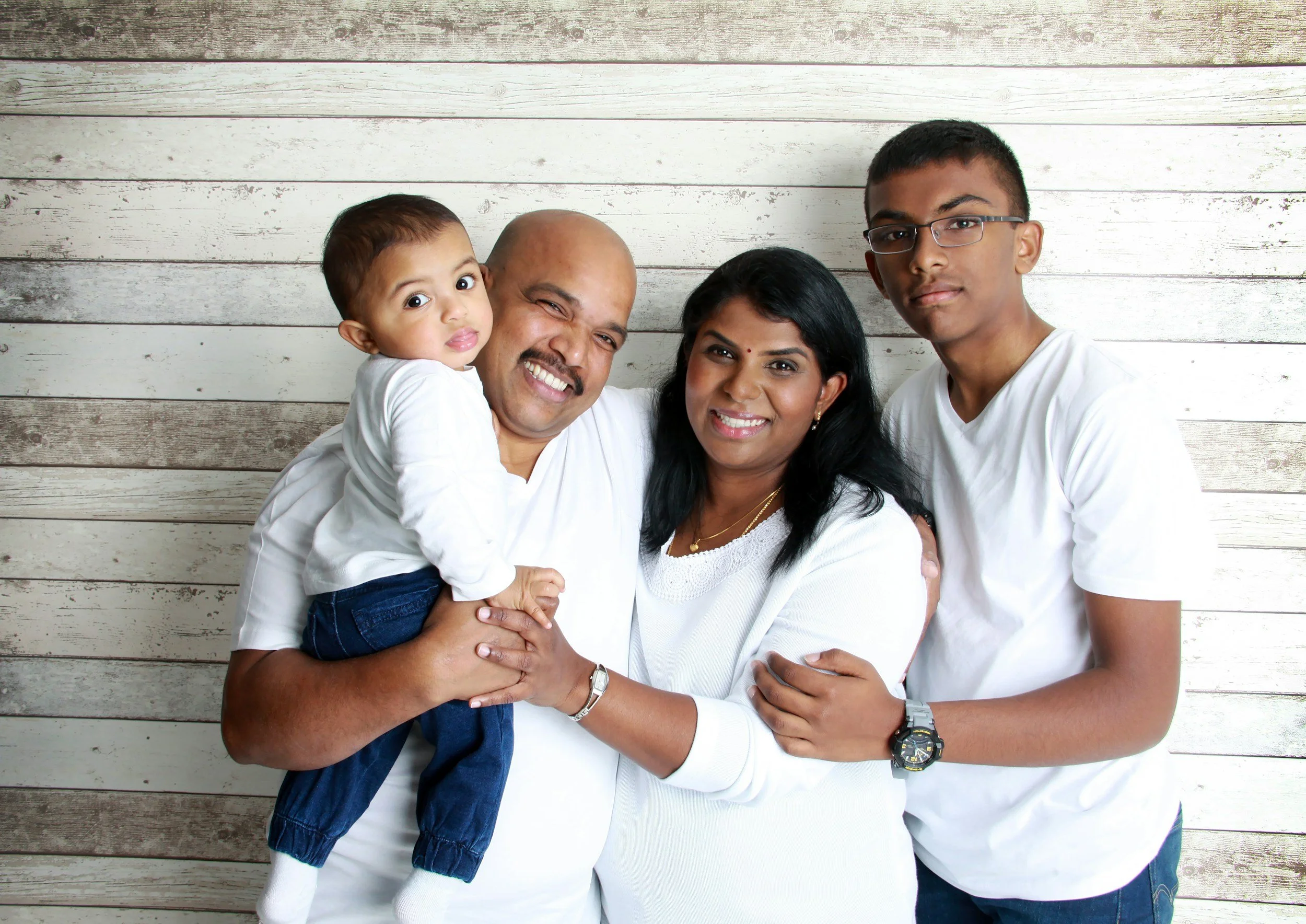 Family with a diverse cultural background stand against a wood-paneled wall.