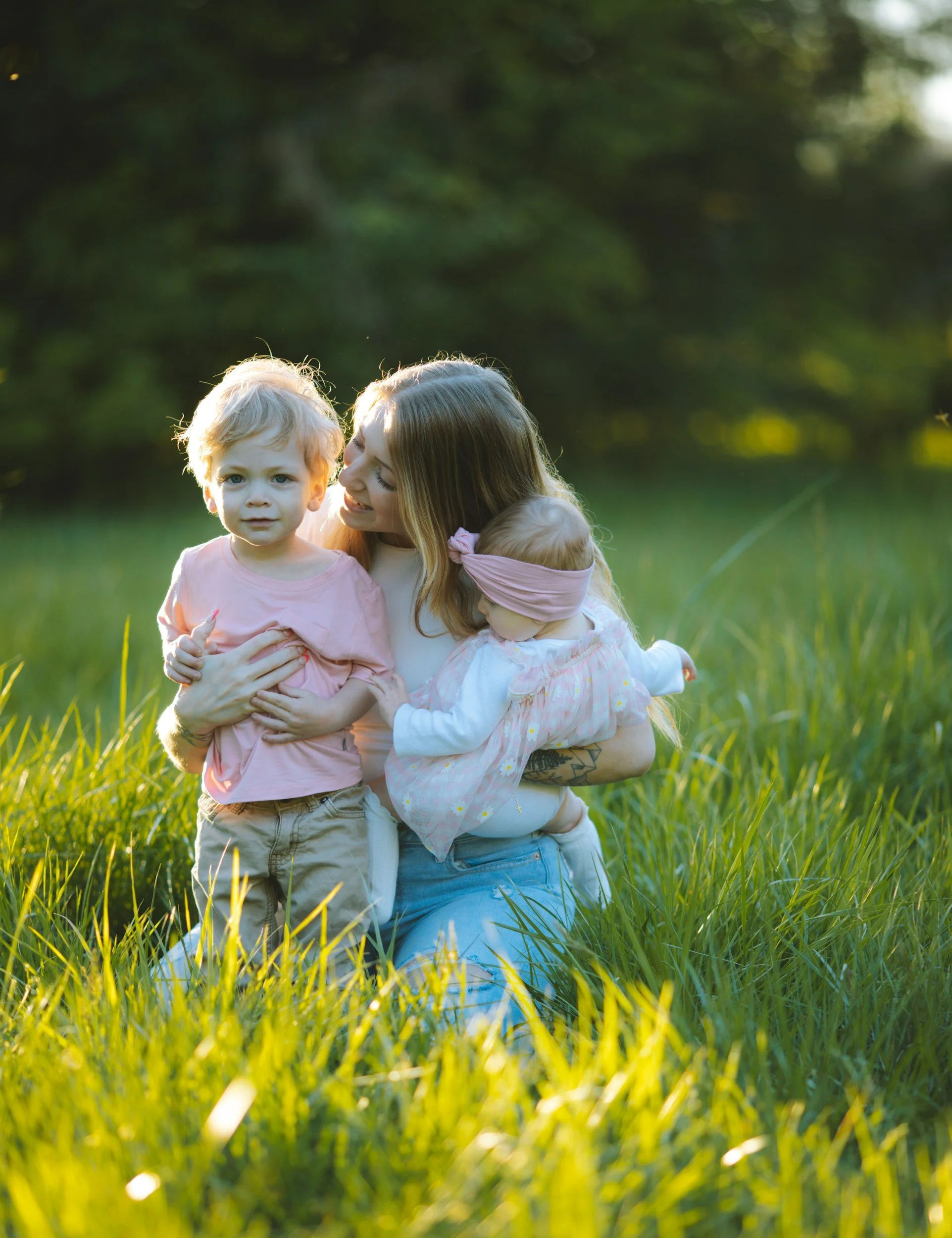 Mother with baby and toddler in field as sun is setting.