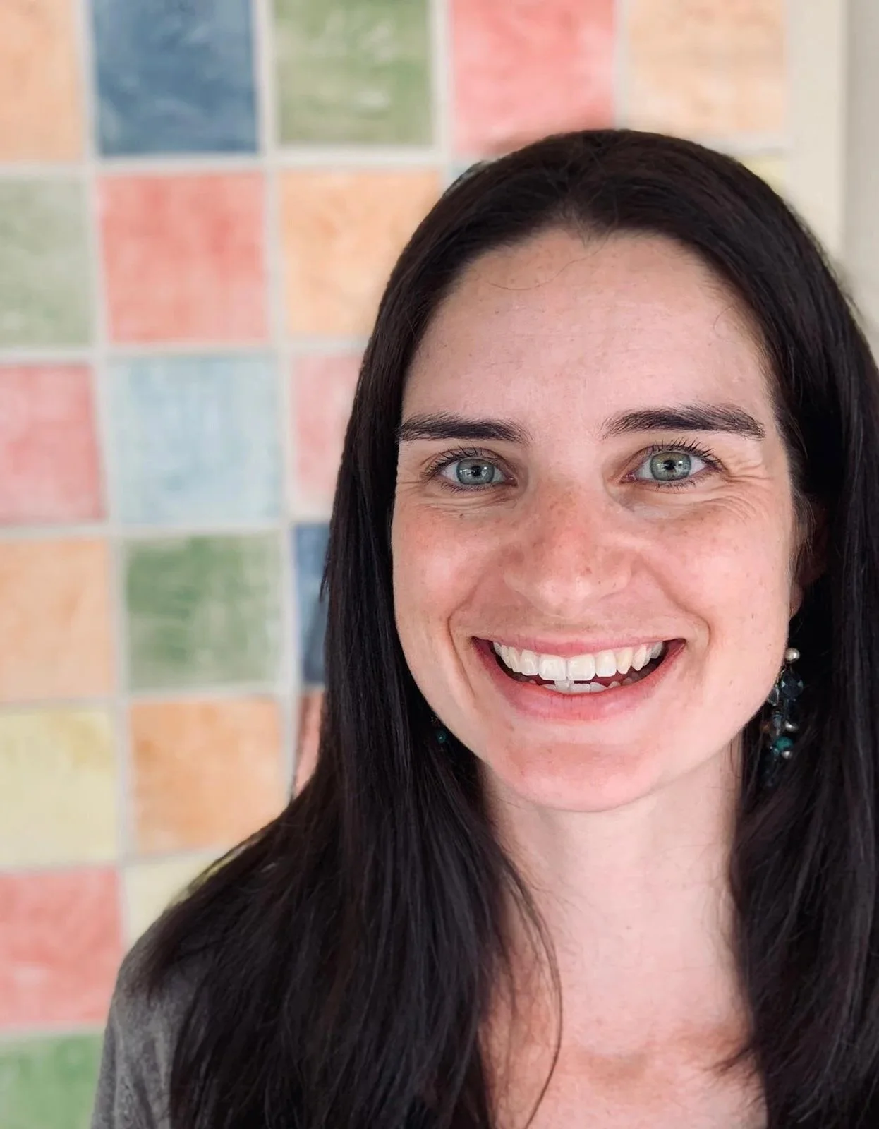 Image of Karen Nitsche, paediatric speech therapist smiling and standing in front of a colourful wall.