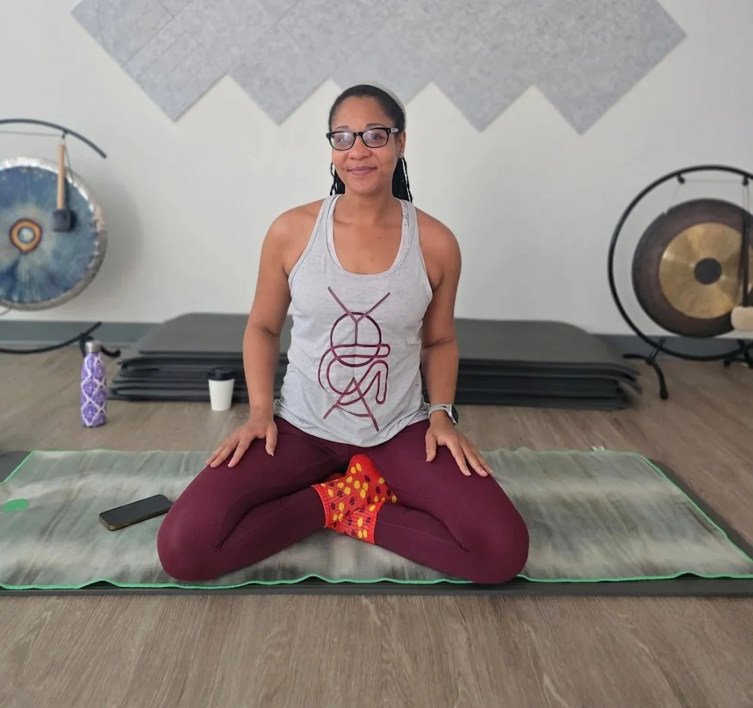 Woman smiling during a yoga pose, leaning forward with her hands clasped together, on a yoga mat.