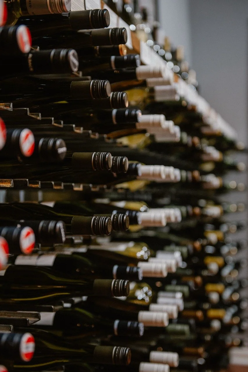 A wall of horizontally stacked wine bottles stored necks inwards in a wine cellar.