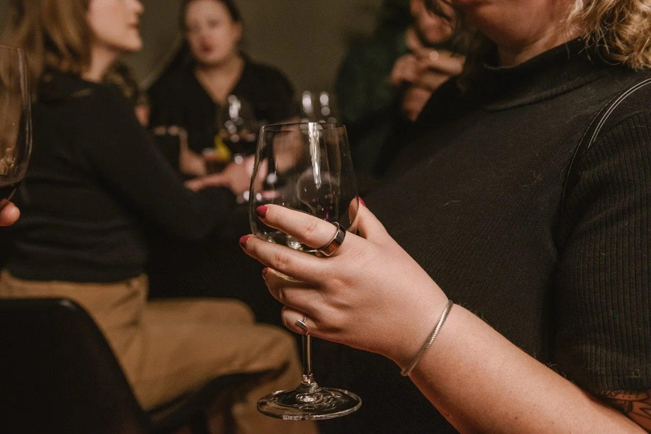 Person holding an empty wine glass at a social gathering with others in the background.