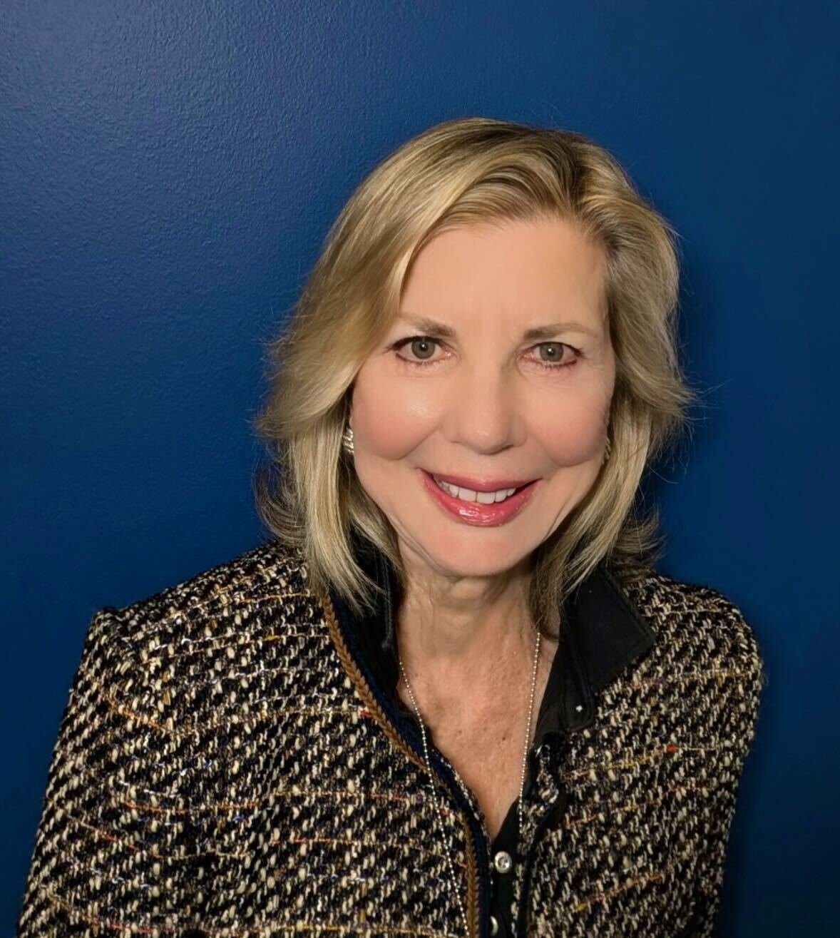 Professional woman smiling in a business suit, posed in front of a neutral background.
