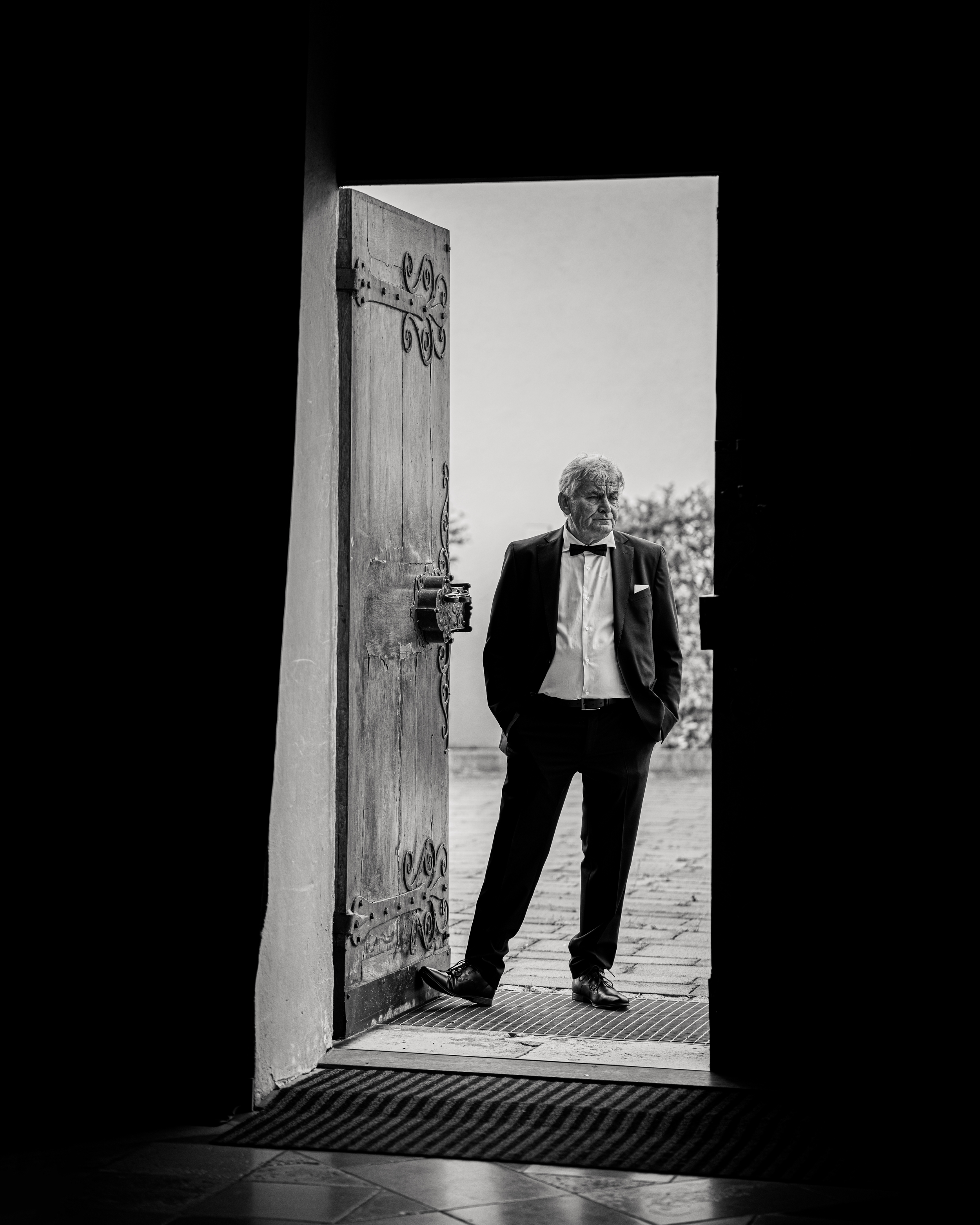 A man in formal attire standing in a doorway, black and white photograph.