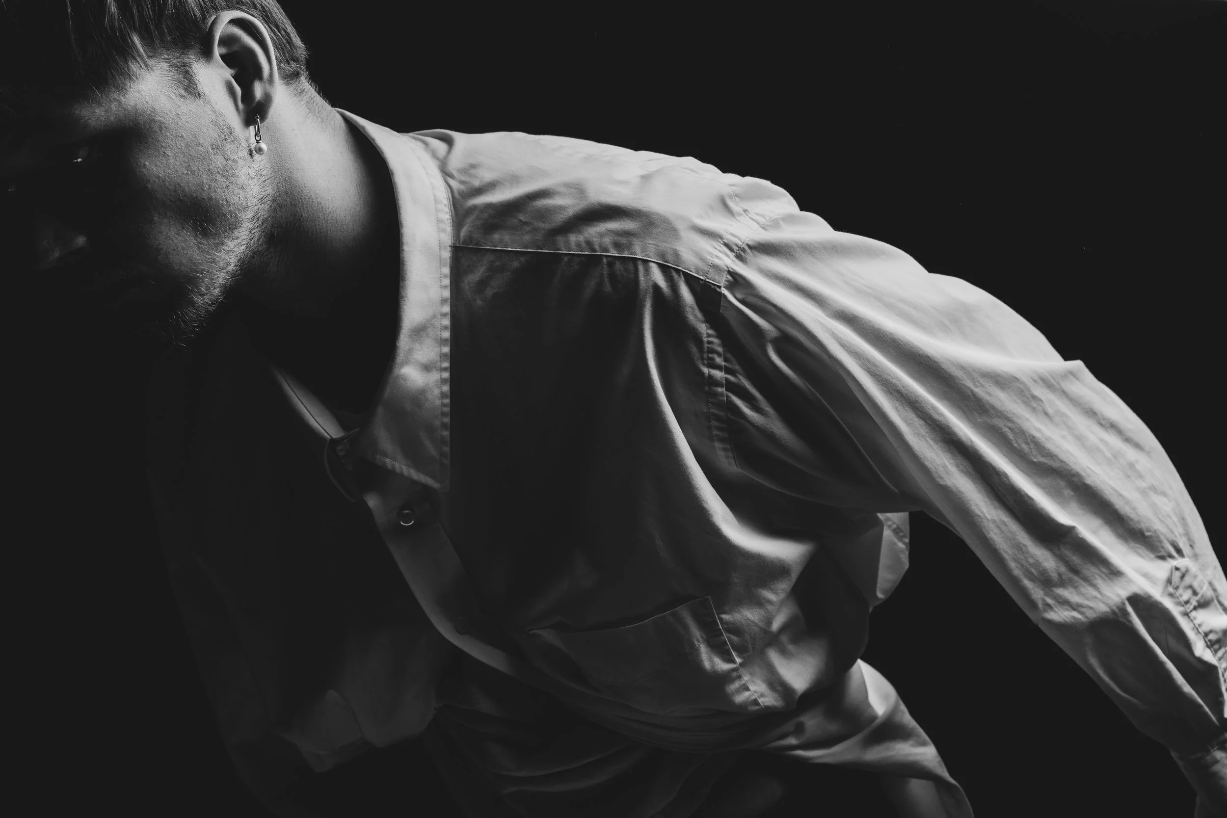 A black and white photo of a man wearing a white shirt, looking downward with a contemplative expression.