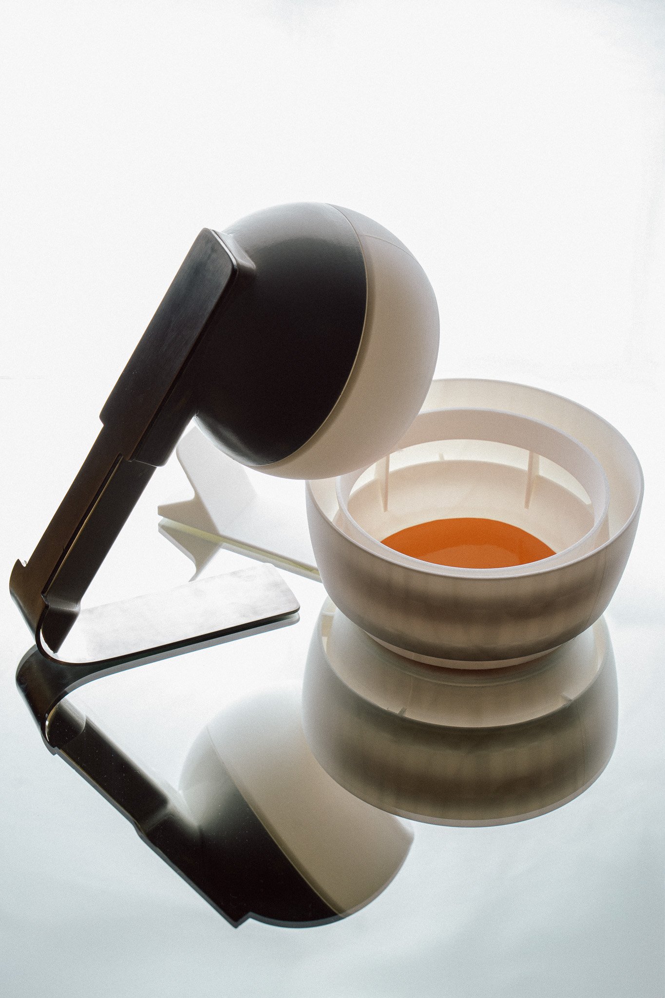 Modern juicer with white and black components, featuring a strainer and bowl containing orange juice, on a reflective surface.