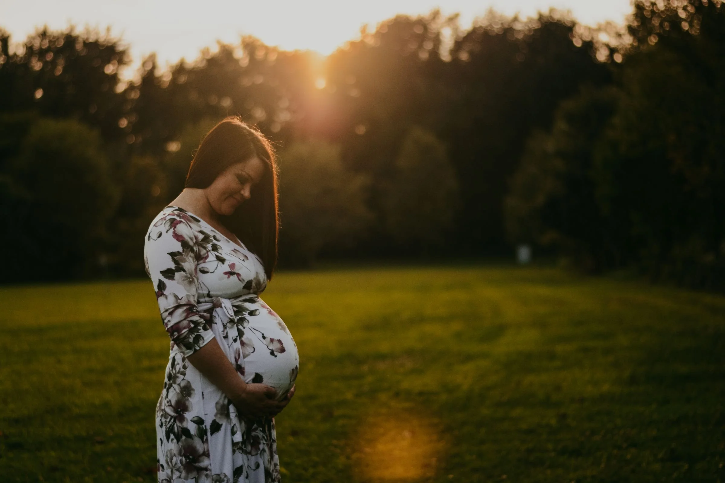 A pregnant woman holding her belly in a green field at sunset.