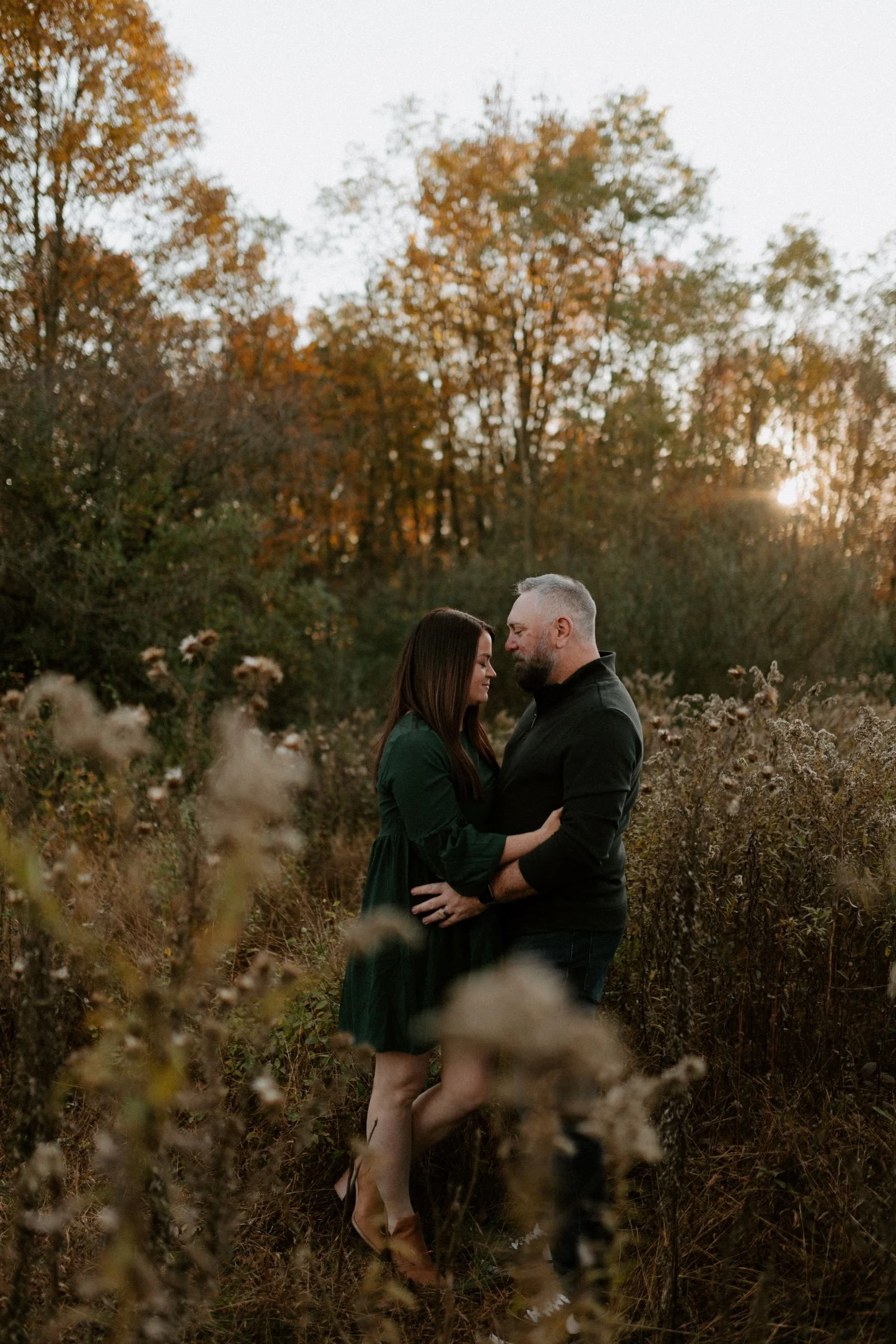 a man and woman looking at each other lovingly while standing in field at sundown