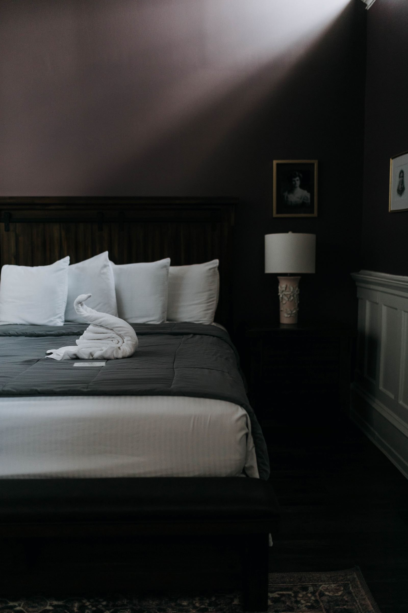 a bed with a towel folded into a swan as light shines down from the window in a lavender boutique hotel room 