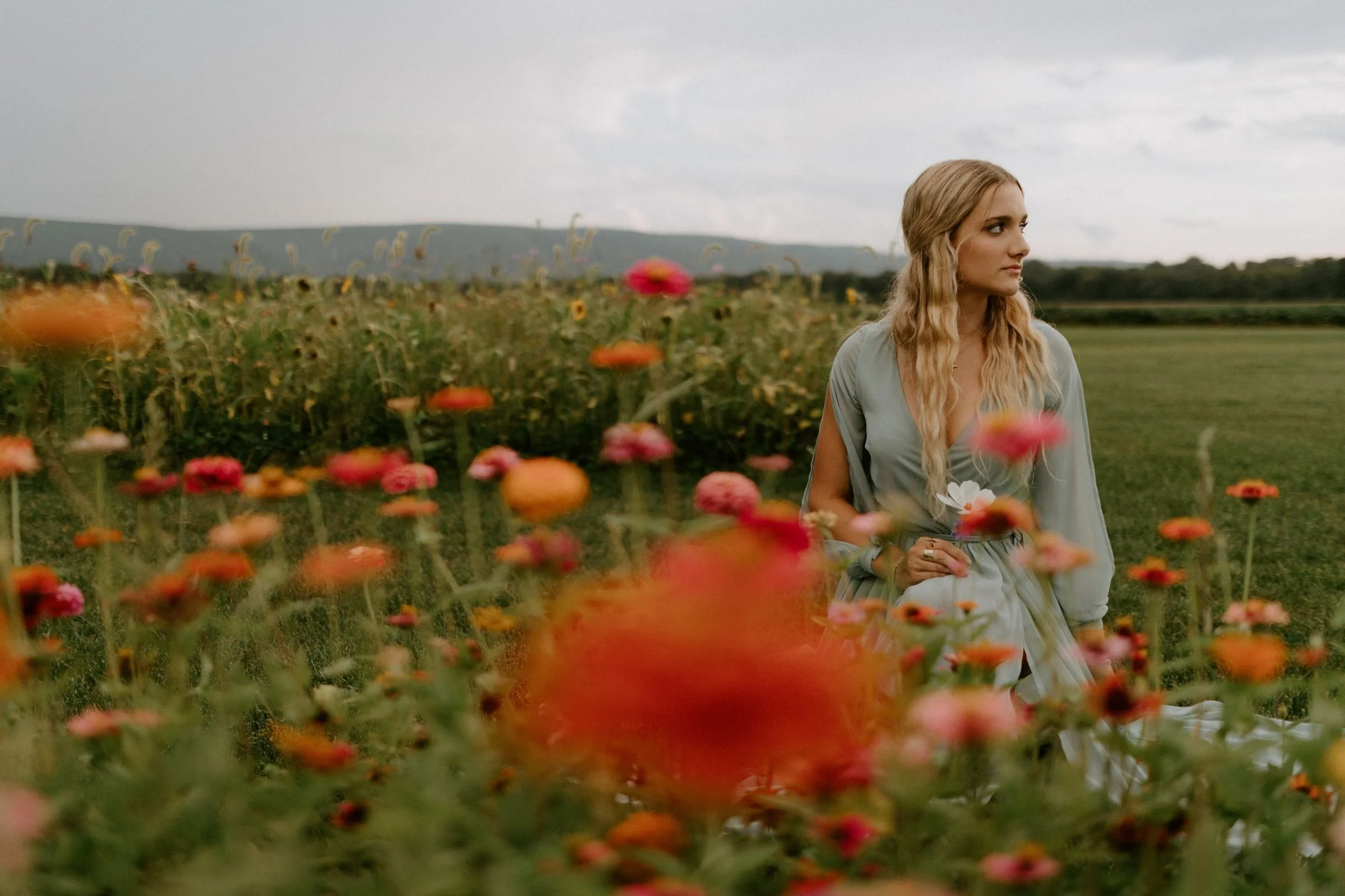 A teenage girl standing in a green field filled with bright orange and red flowers for her senior session in Montoursville, Pennsylvania