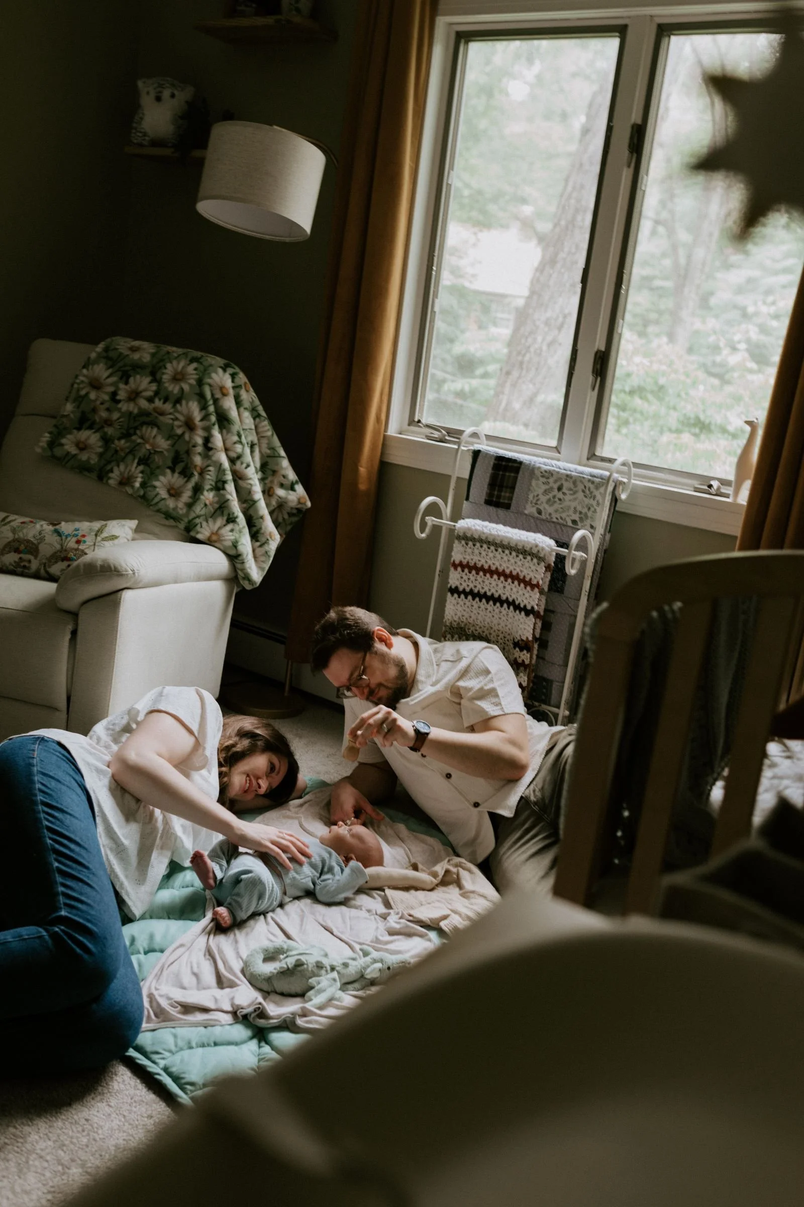 Mother, father and newborn lying on the floor playing together on a baby blanket during a documentary style family session in Williamsport, Pennsylvania.