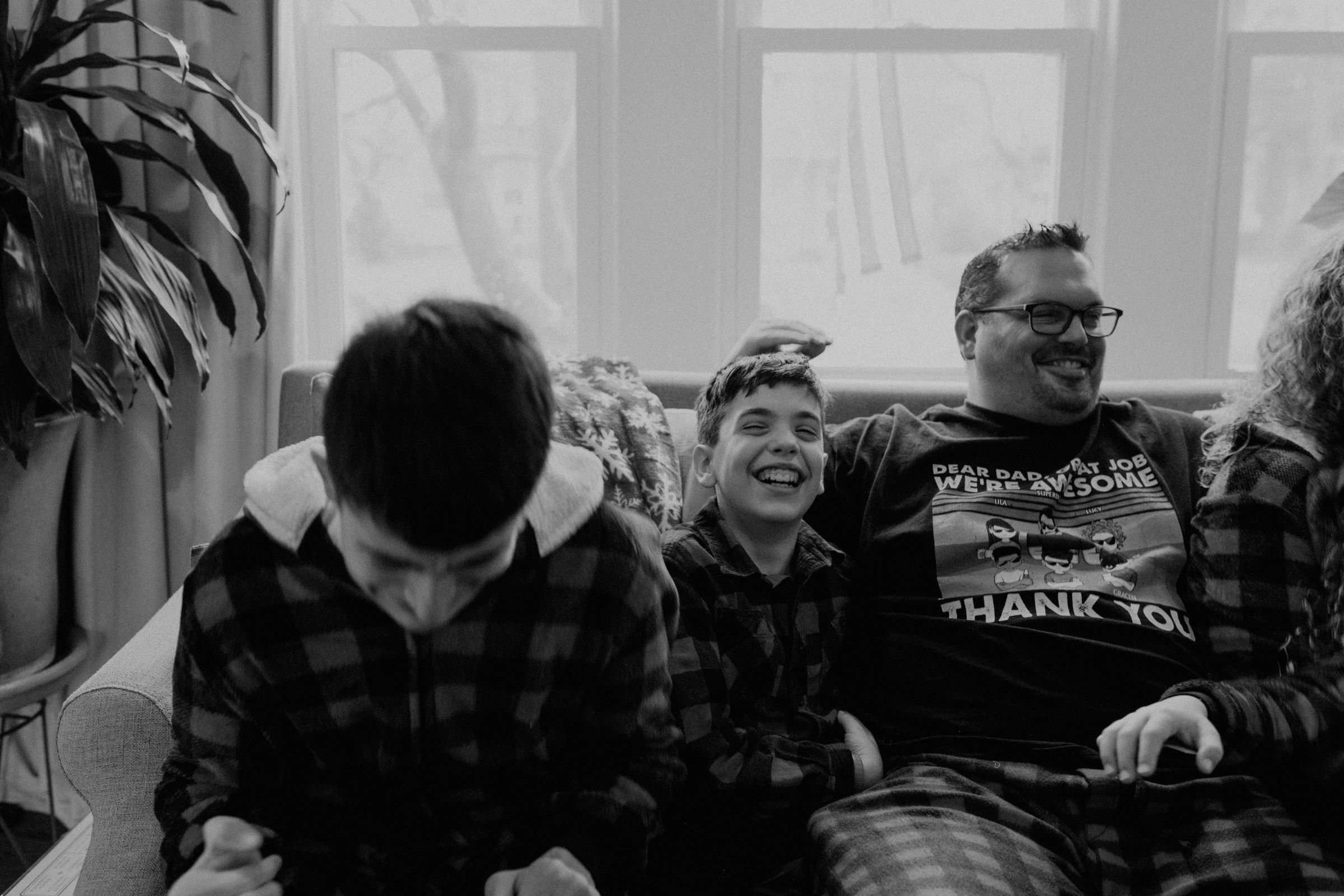 a father laughing with two teenage sons on a couch, dressed in matching buffalo plaid pajamas
