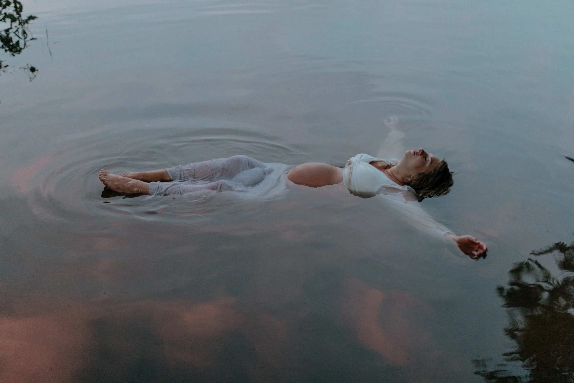 A pregnant woman floating in the Susquehanna river with pink clouds reflecting in the water in Lewisburg, Pennsylvania.